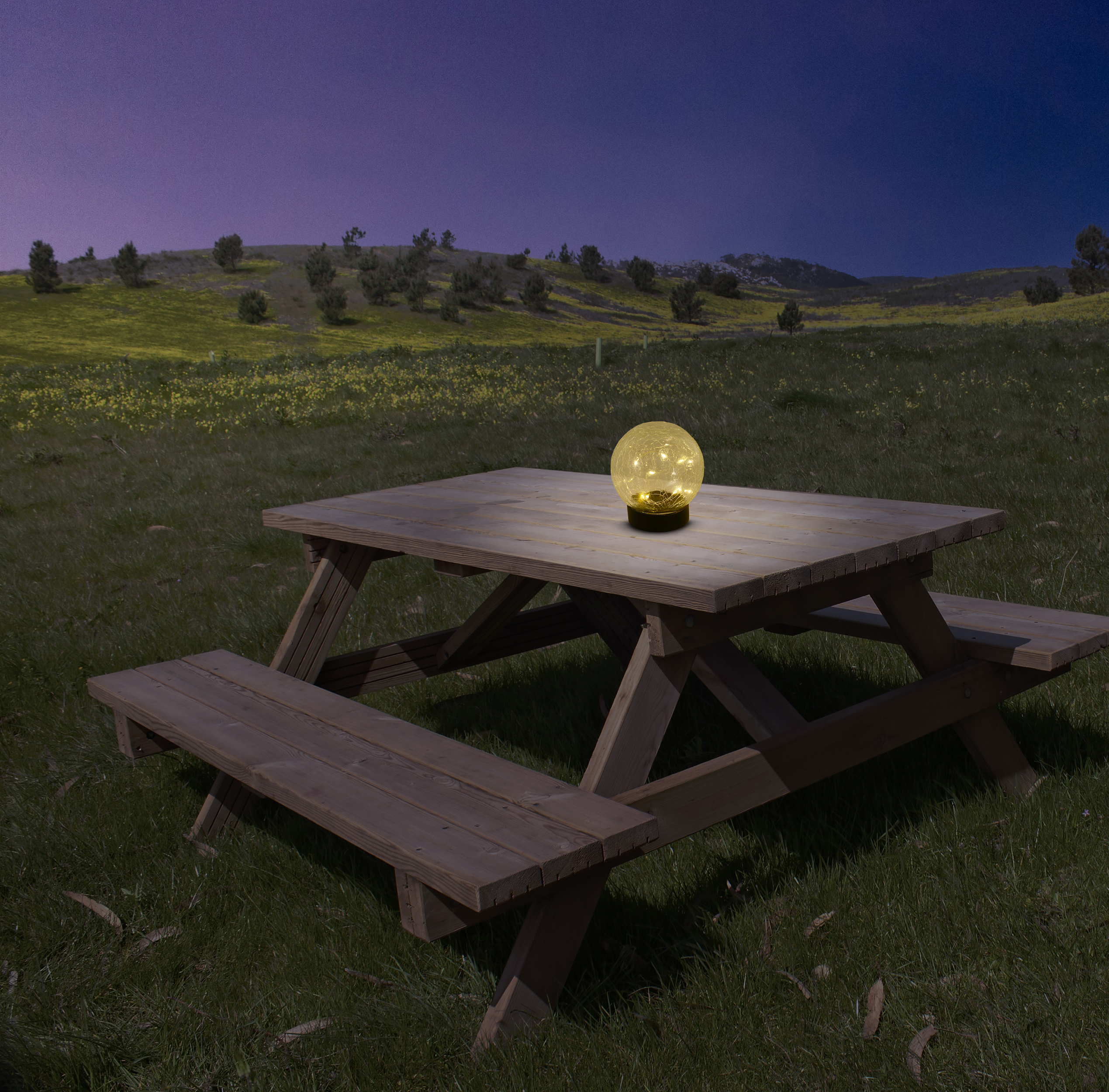 Ein Picknicktisch aus Holz mit einer leuchtenden, kugelförmigen Lampe bei Nacht.