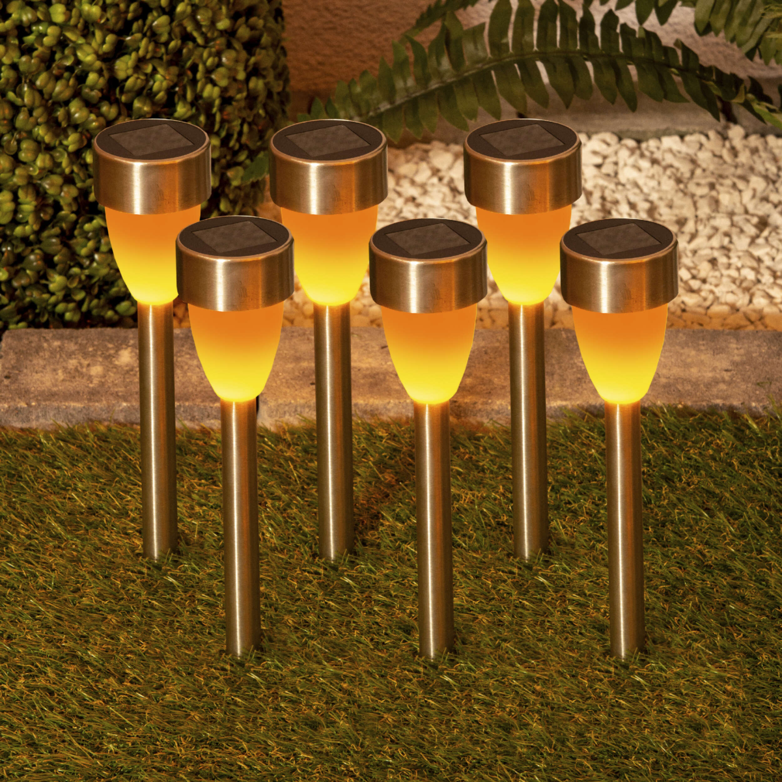 Sechs Solar-Gartenleuchten auf Gras. Sie haben einen silbernen Aufsatz und ein gelbes Leuchtlicht.
