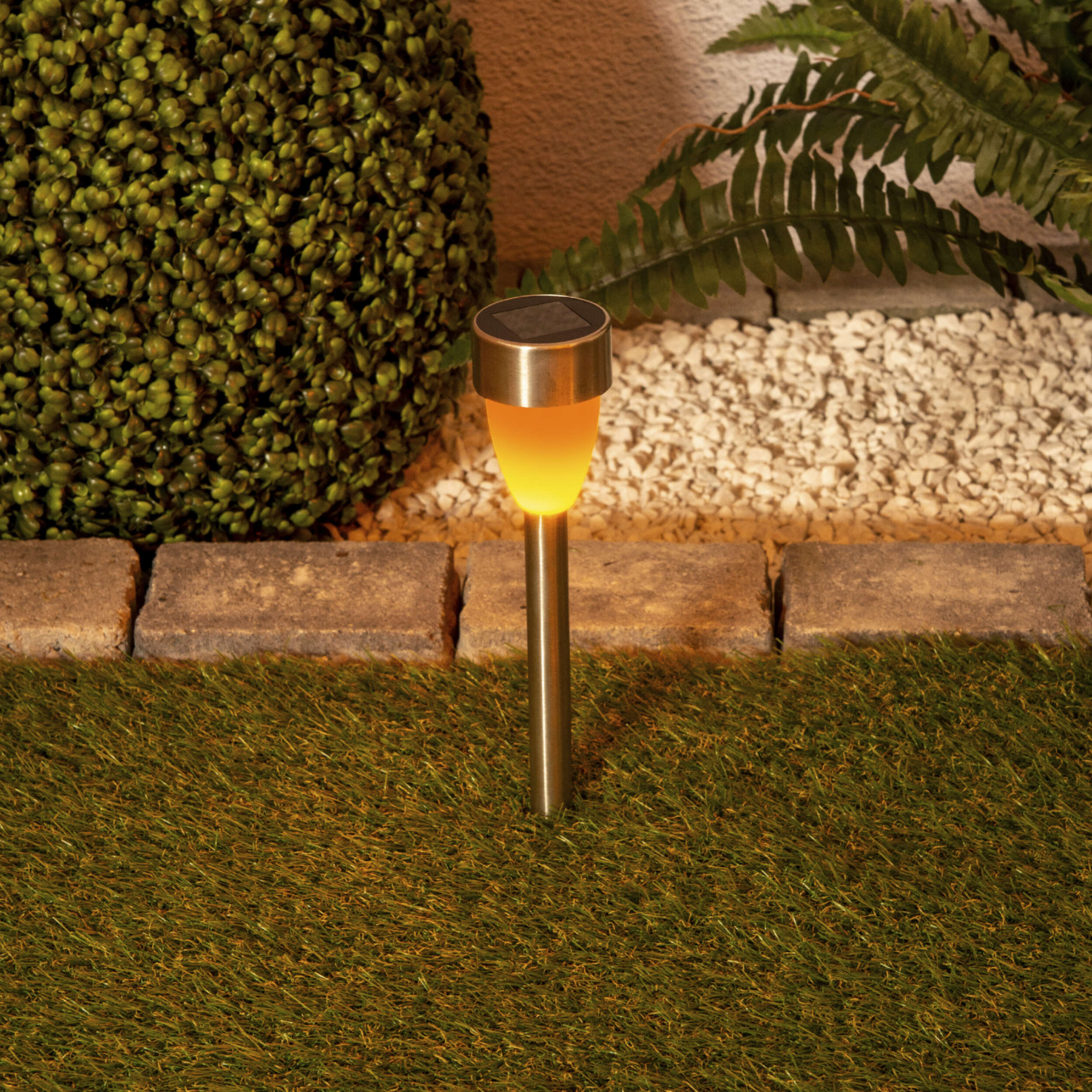 Solar-Gartenlicht, das gelb leuchtet, im Gras gepflanzt, mit Grün im Hintergrund.