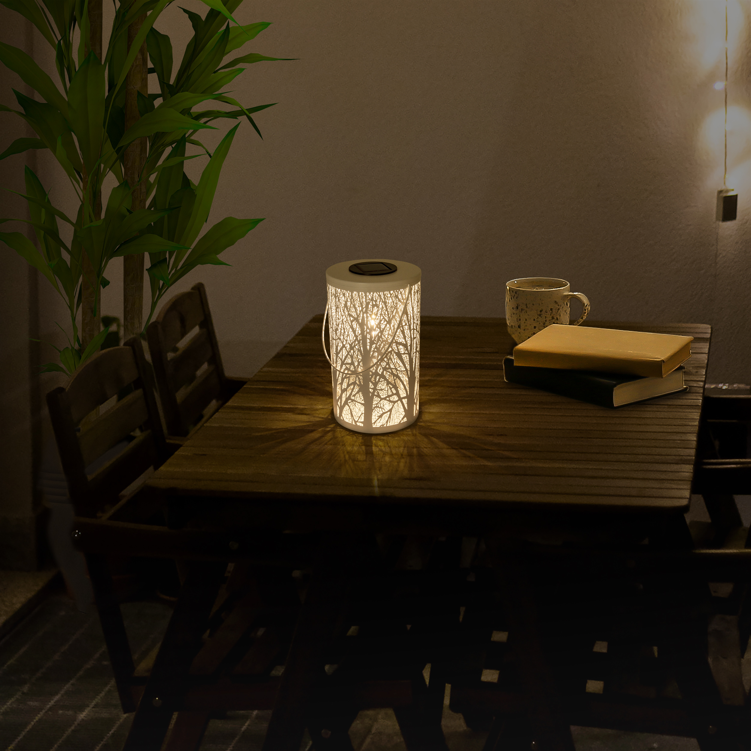 Eine weiße Laterne mit Baumdesign auf einem Holztisch, mit einer Tasse und Büchern.