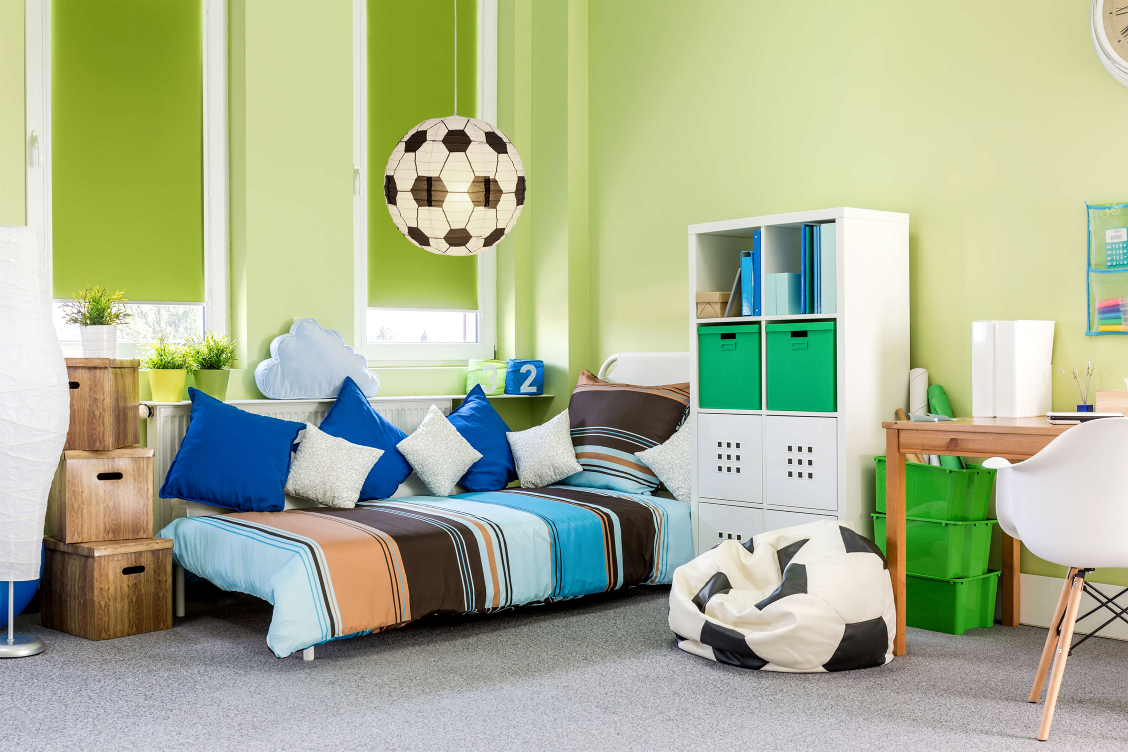 Ein grünes Zimmer mit Bett, Sitzsack und Fußball-Leuchte.