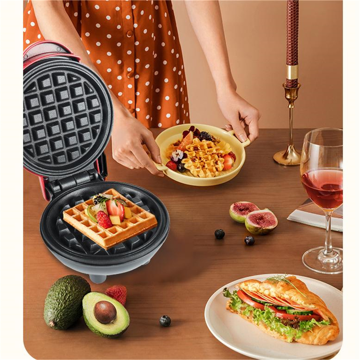 Waffeleisen mit Waffel und Obst. Eine Person hält einen Teller mit Waffeln.