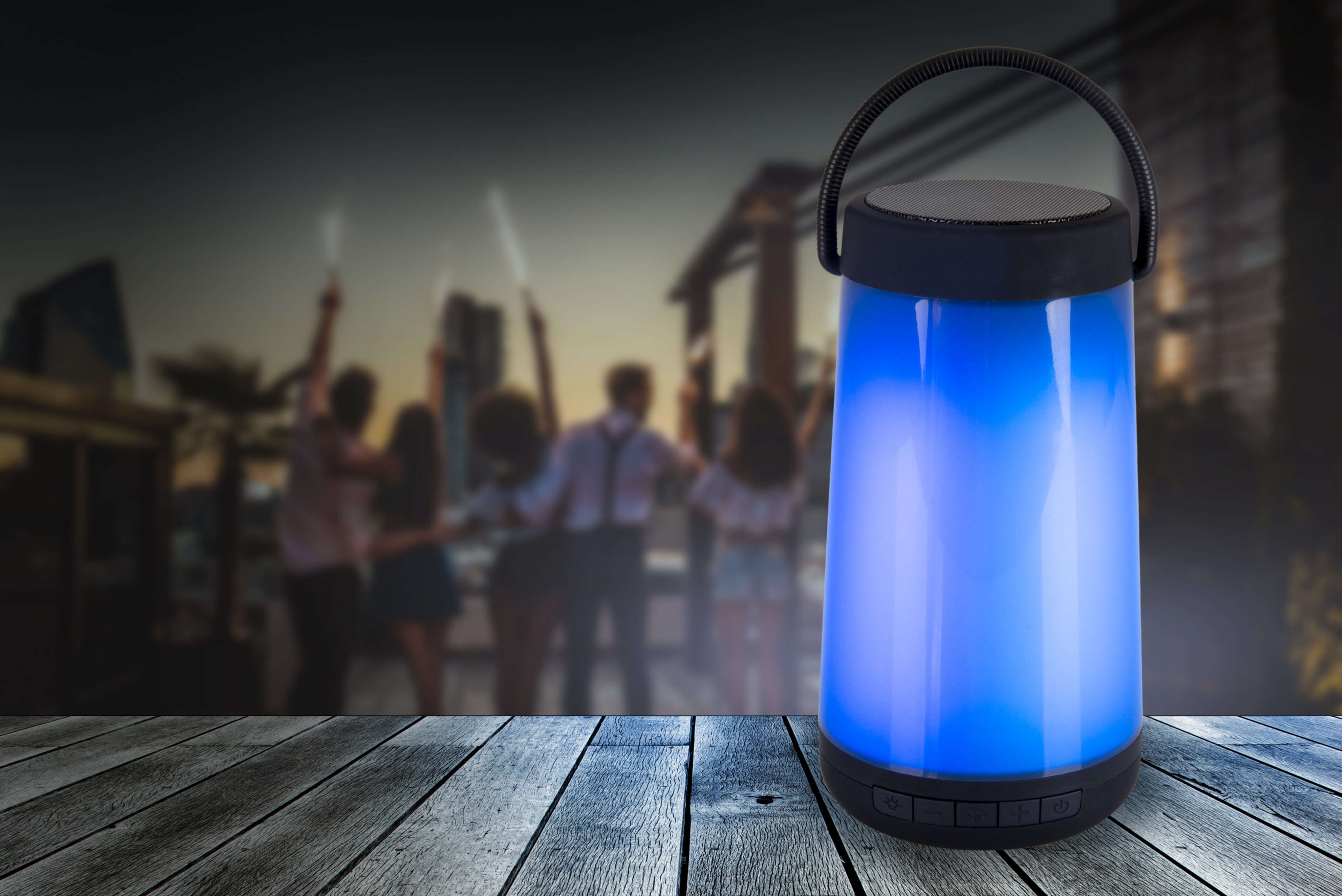 Ein blauer Lautsprecher mit Lichtern auf einem Holzdeck und eine Party im Hintergrund.