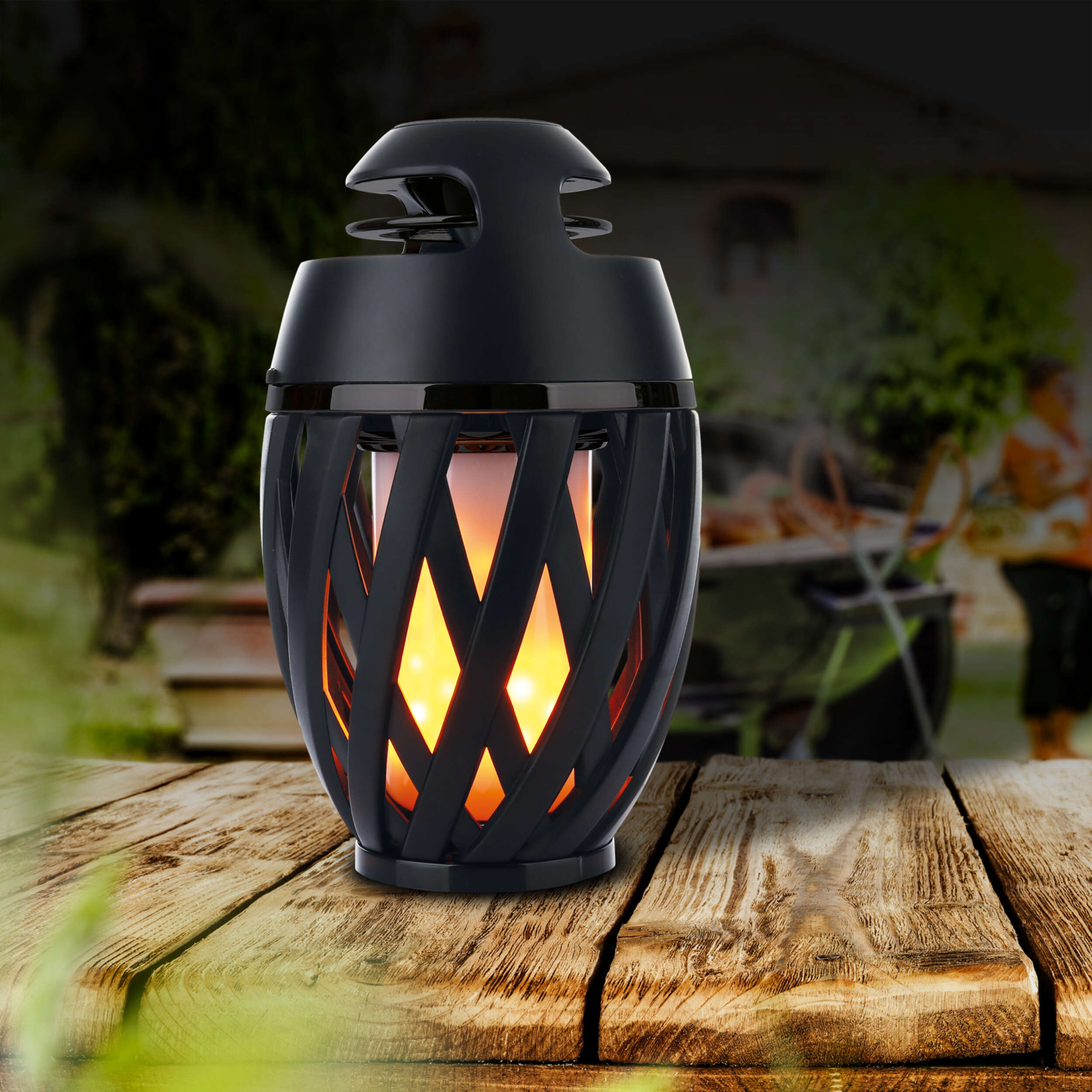 Schwarze Laterne mit Flammeneffekt auf einem Holztisch. Verschwommener Hintergrund im Freien.