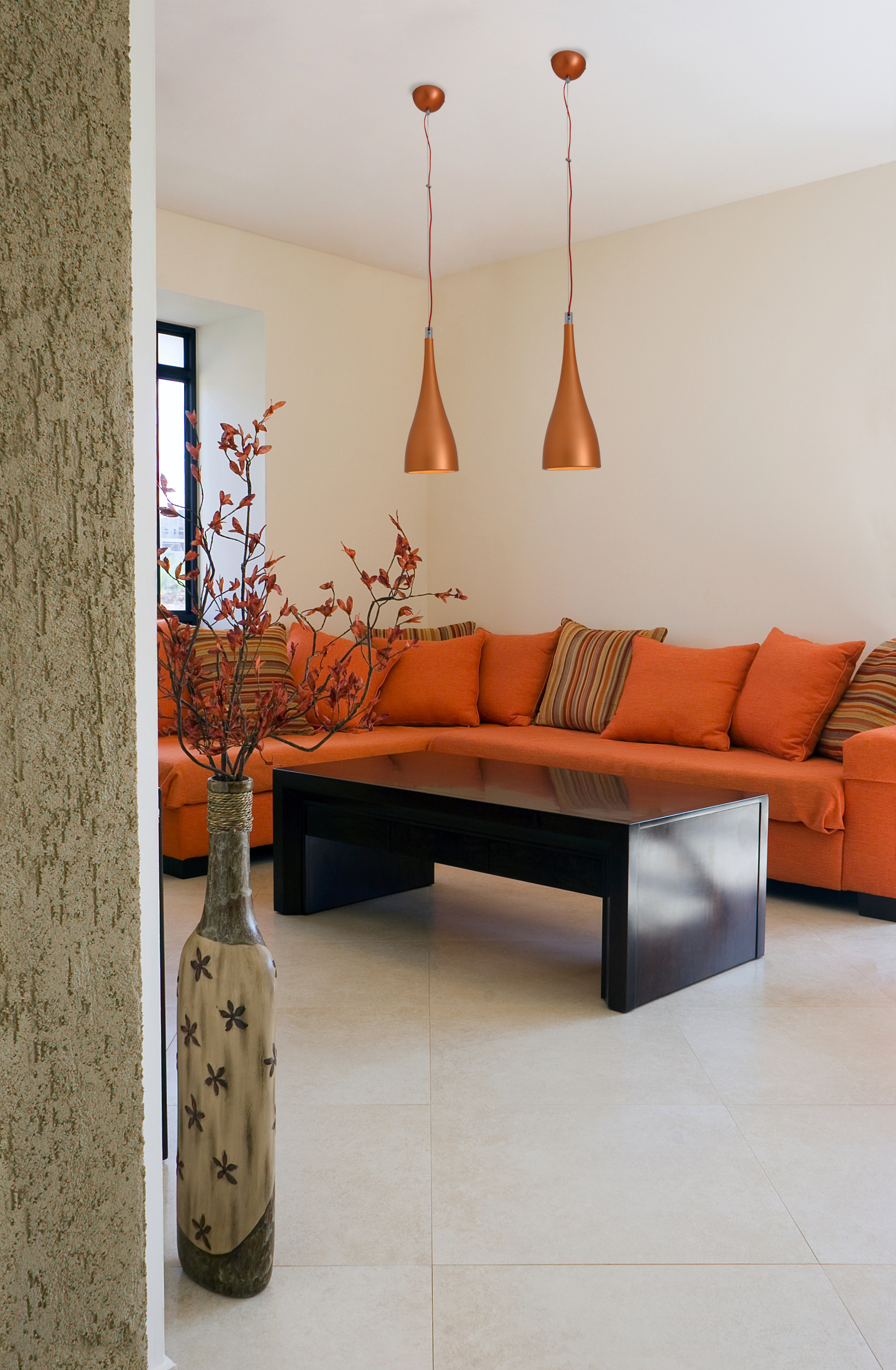 Wohnzimmer mit orangefarbenem Sofa, schwarzem Tisch, Pendelleuchten und Blumenvase. Beige Wände.