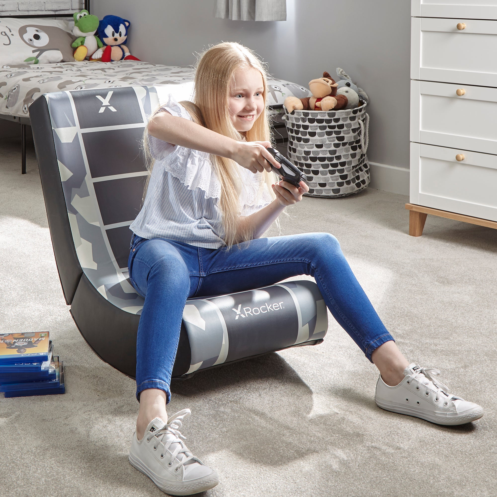 Mädchen spielt Videospiel in Gaming-Stuhl. Spielzeug und Bett im Hintergrund. Lächelt.