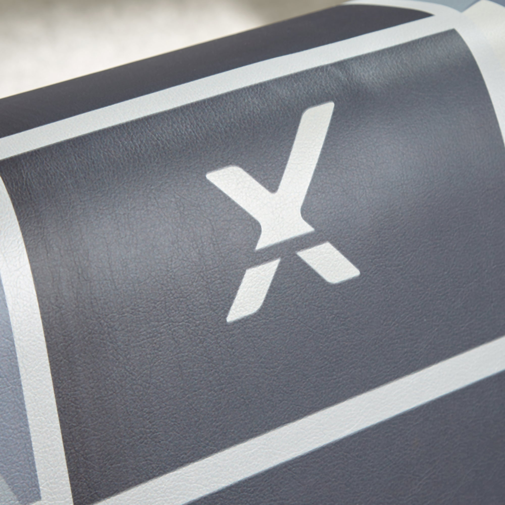 Nahaufnahme einer Oberfläche mit einem weißen 'X' Logo auf grauem und schwarzem Hintergrund mit weißen Streifen.