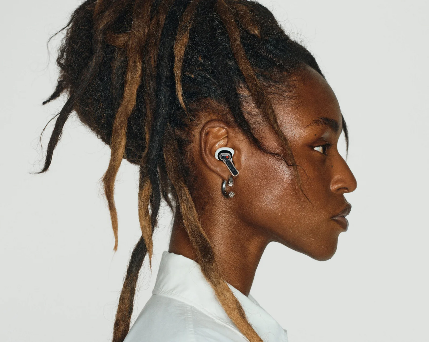 Eine Person mit Dreadlocks trägt ein weißes Hemd und einen Ohrhörer im Ohr.