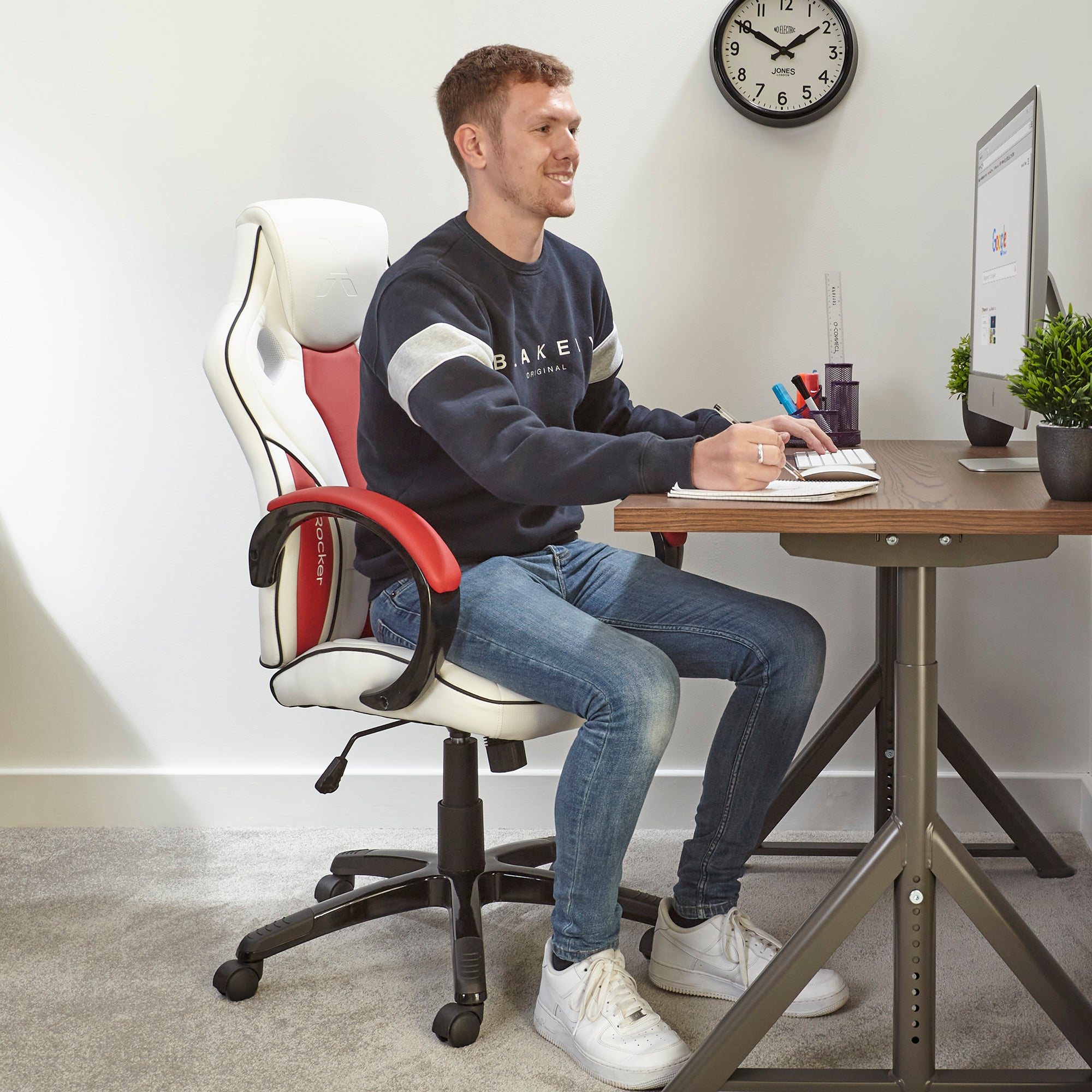 Ein Mann arbeitet an einem Schreibtisch vor einem Computer und sitzt in einem Gaming-Stuhl.