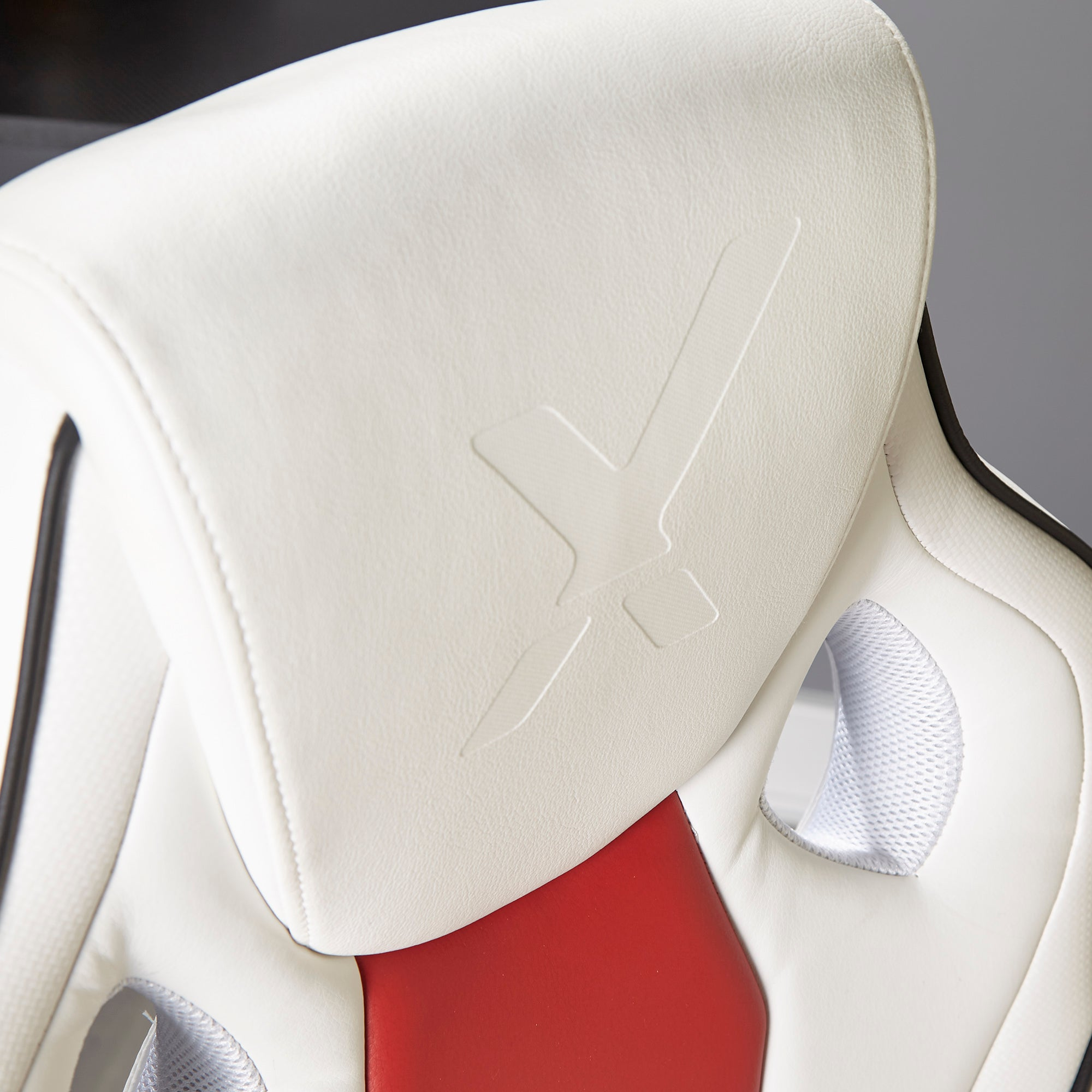 Nahaufnahme der Kopfstütze eines weiß-roten Gaming-Stuhls mit geprägtem Logo und Mesh-Details.