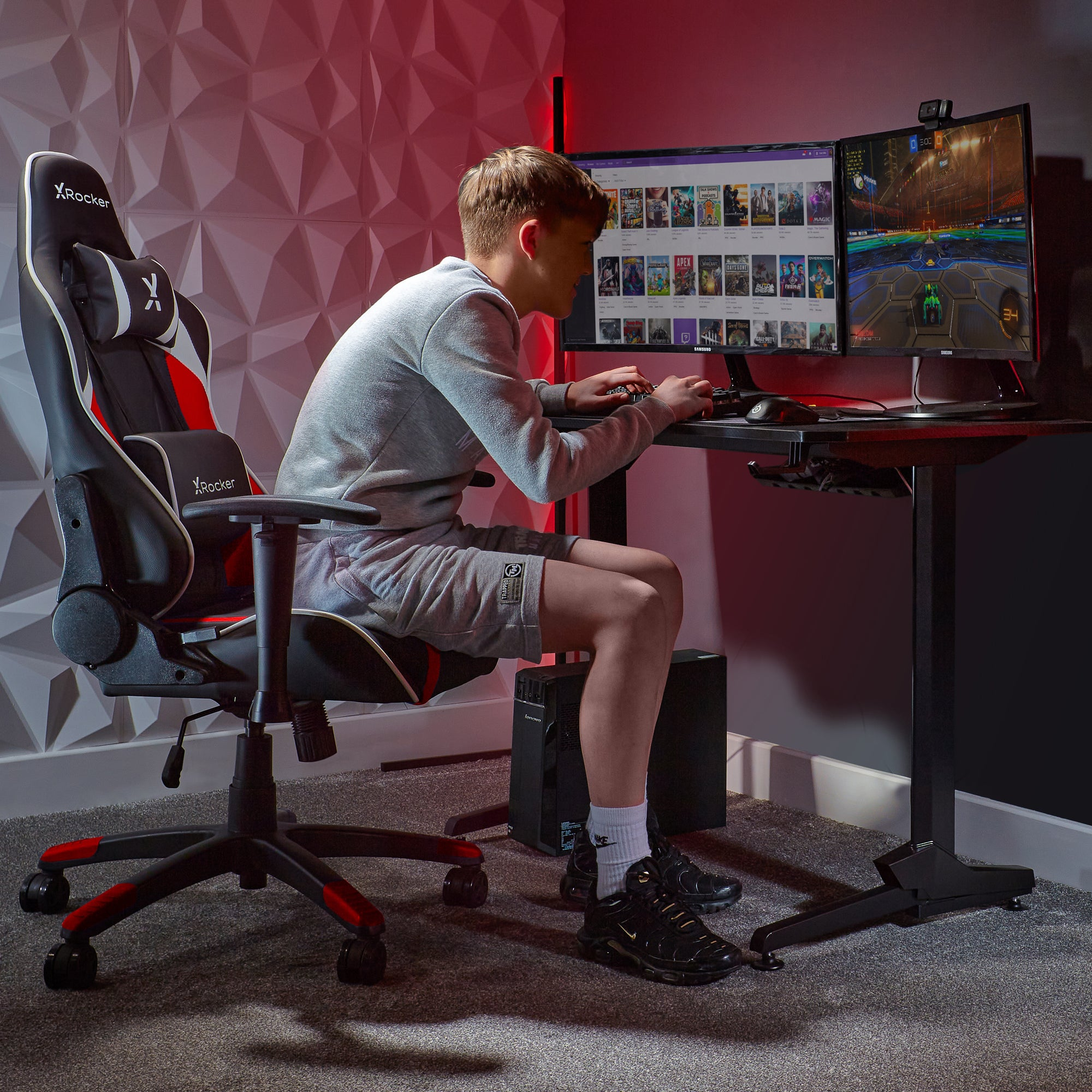 Ein Junge spielt ein Spiel auf zwei Monitoren. Er sitzt in einem schwarz-roten Gaming-Stuhl.