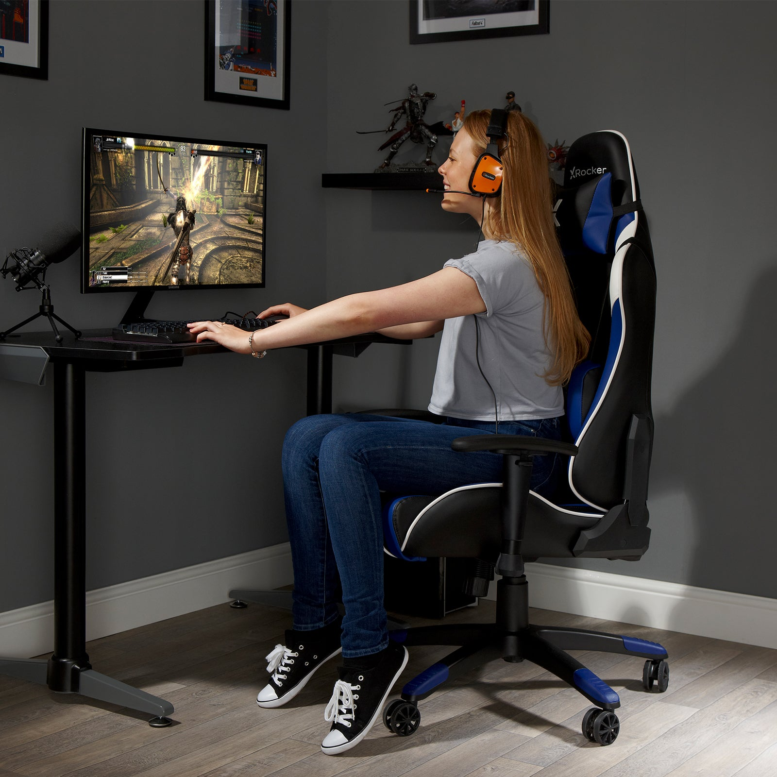 Frau spielt an einem Schreibtisch mit Monitor. Trägt ein Headset und einen Gaming-Stuhl.