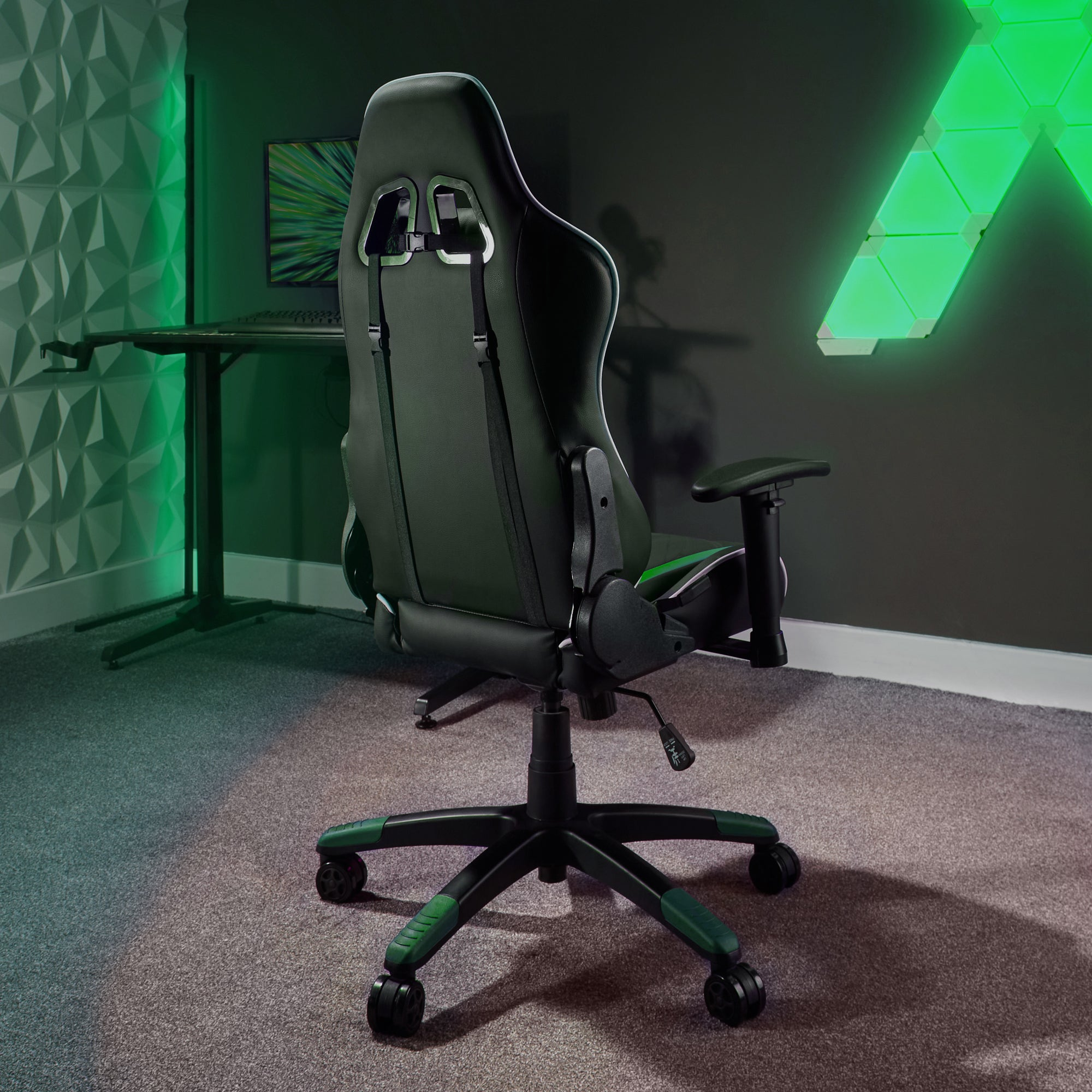 Ein grüner Gaming-Stuhl von hinten. Er steht auf einem grauen Teppich, mit einem Schreibtisch und Lichtern im Hintergrund.