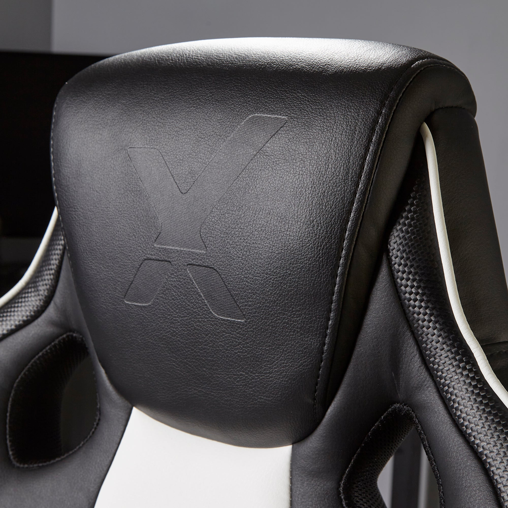 Nahaufnahme der Kopfstütze eines Gaming-Stuhls. Schwarzes Leder mit weißem Streifen und großem 'X'-Logo.