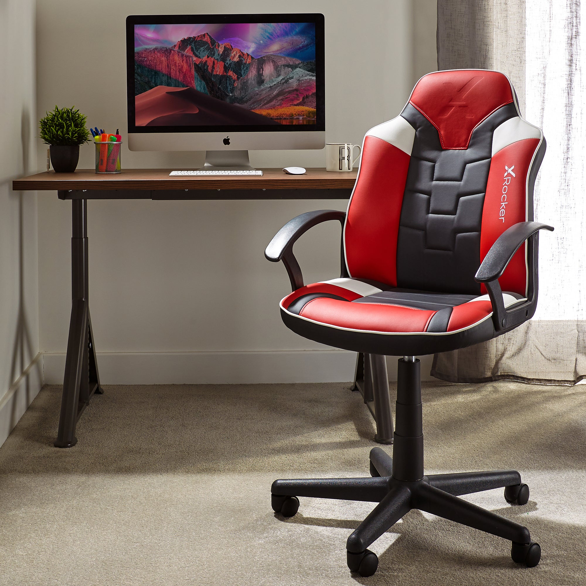 Gaming-Setup mit rotem/schwarzem Stuhl, Schreibtisch und Monitor. Pflanze und Stifte.