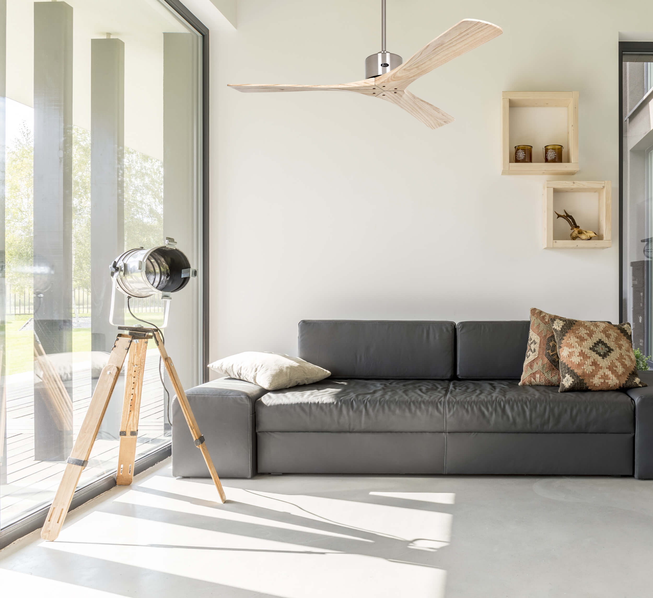 Soggiorno moderno con divano grigio, ventilatore a soffitto in legno e lampada a treppiede. Muri bianchi.