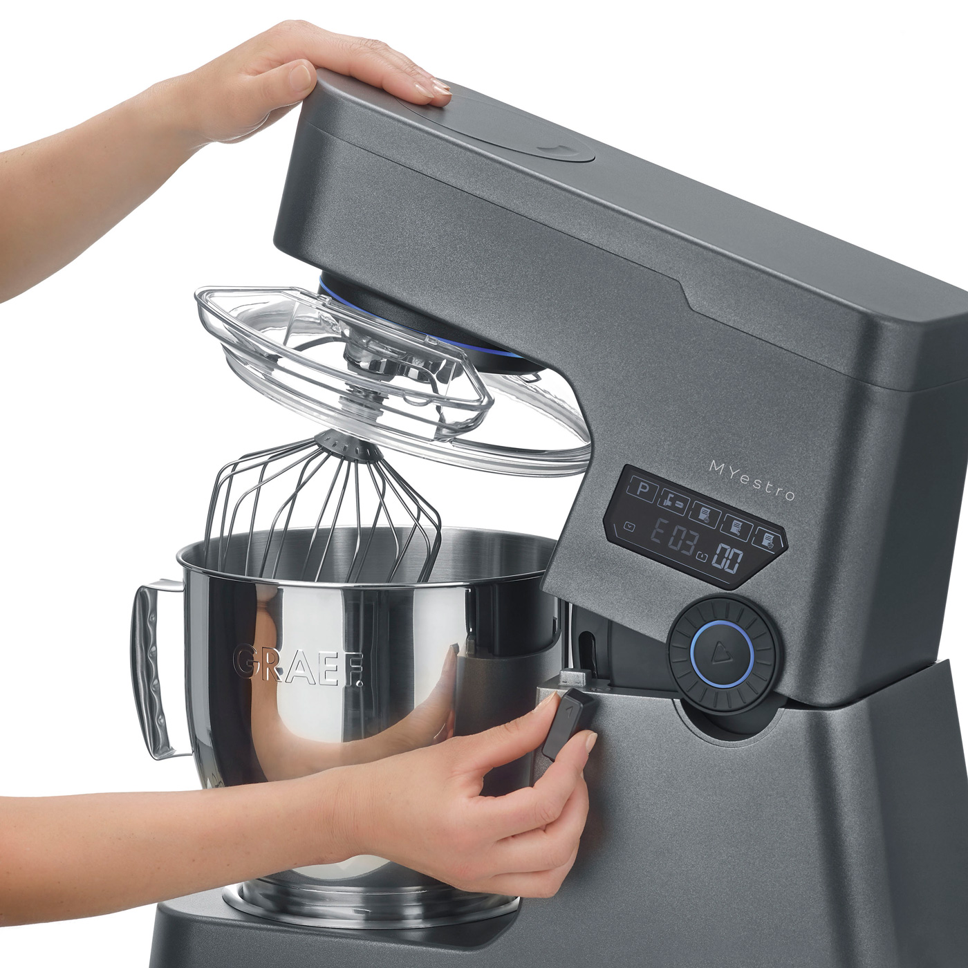 Eine Frau bedient einen grauen Küchenmixer. Der Mixer hat eine silberne Schüssel und einen Deckel.