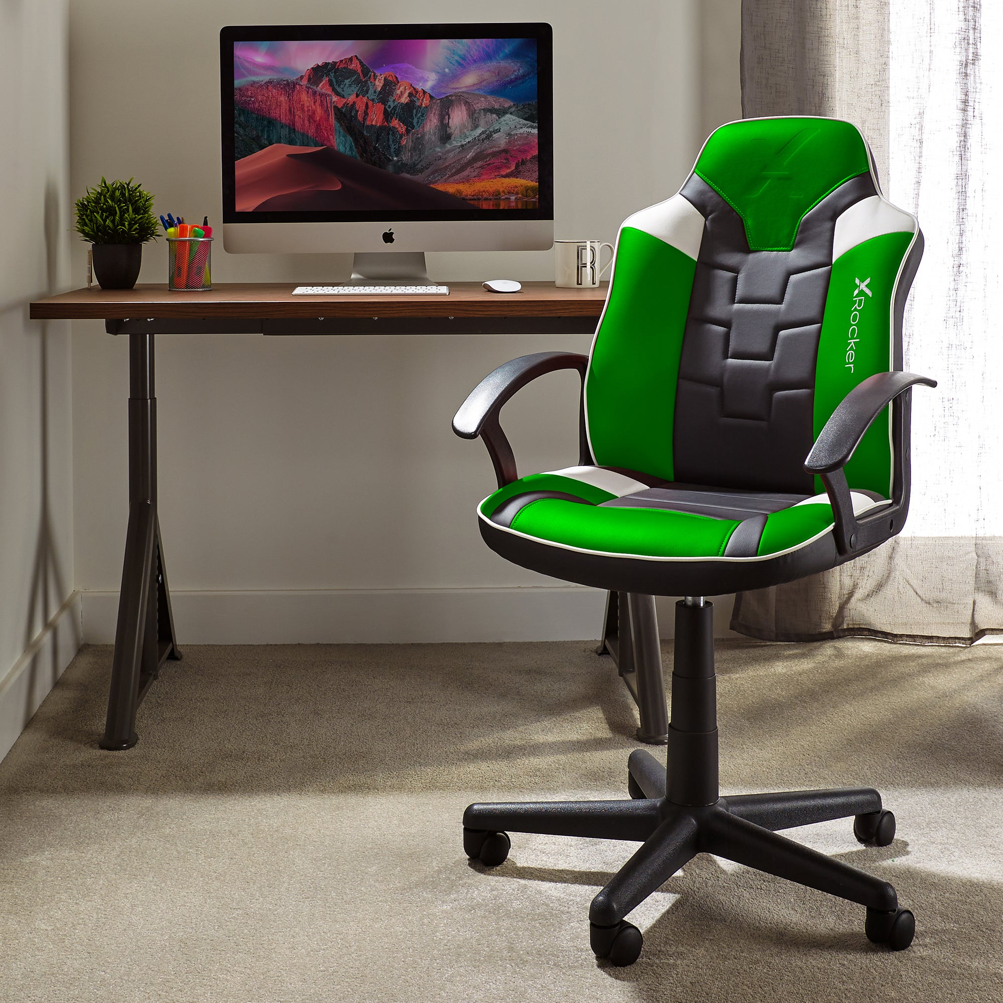 Ein grün-schwarzer Gaming-Stuhl neben einem Schreibtisch mit Computer. Der Raum hat Teppich und ein Fenster.