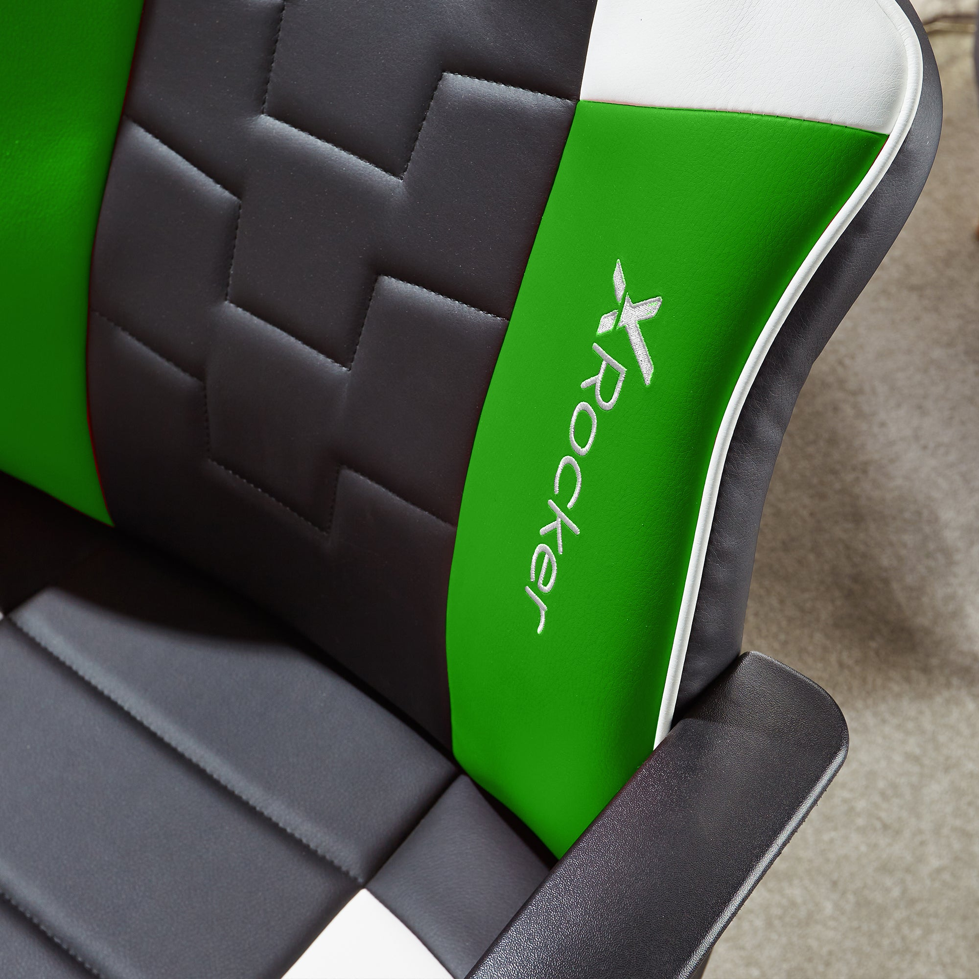 Nahaufnahme eines grün-schwarz-weißen Gaming-Stuhls mit dem X Rocker-Logo. Der Stuhl steht auf grauem Teppich.