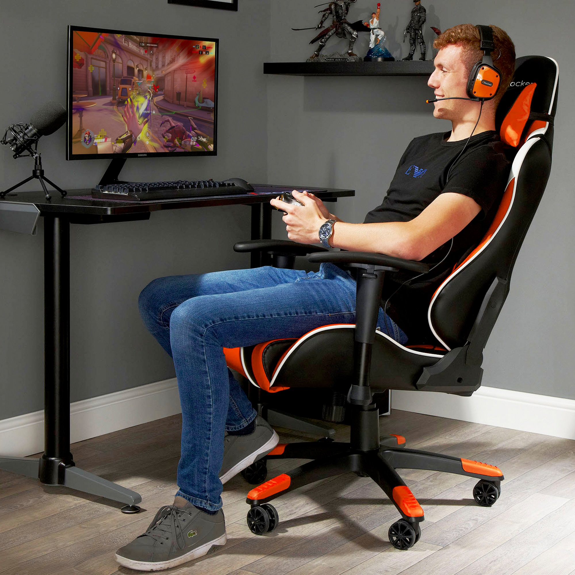 Mann spielt am Computer, sitzt in einem orange-schwarzen Stuhl, mit Headset auf.