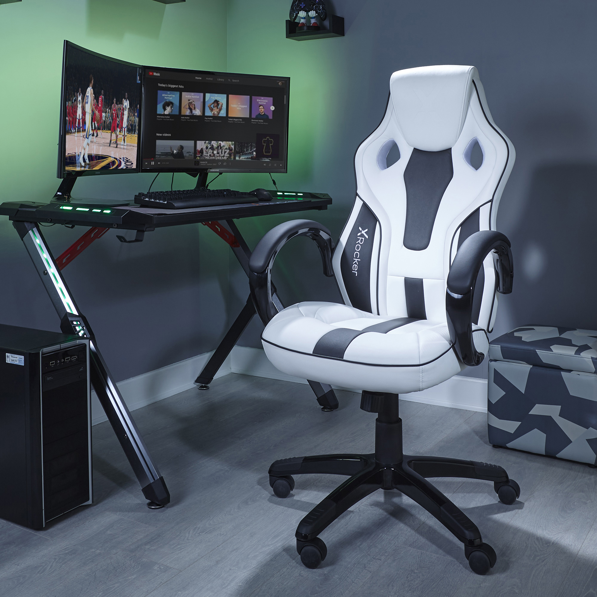 Gaming-Setup: weißer und schwarzer Stuhl, Doppelbildschirme, schwarzer Schreibtisch, PC und eine Camouflage-Aufbewahrungsbox.
