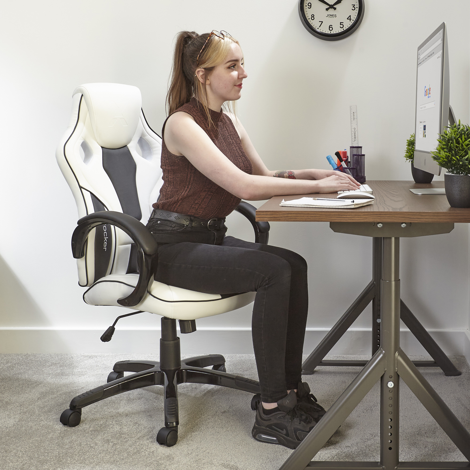 Frau sitzt am Schreibtisch, benutzt Computer, mit Gaming-Stuhl.
