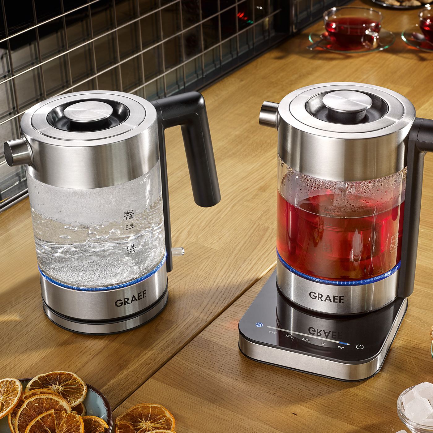 Dwa elektryczne czajniki ze stali nierdzewnej, jeden na wodę, drugi na czerwoną herbatę, na drewnianej powierzchni.