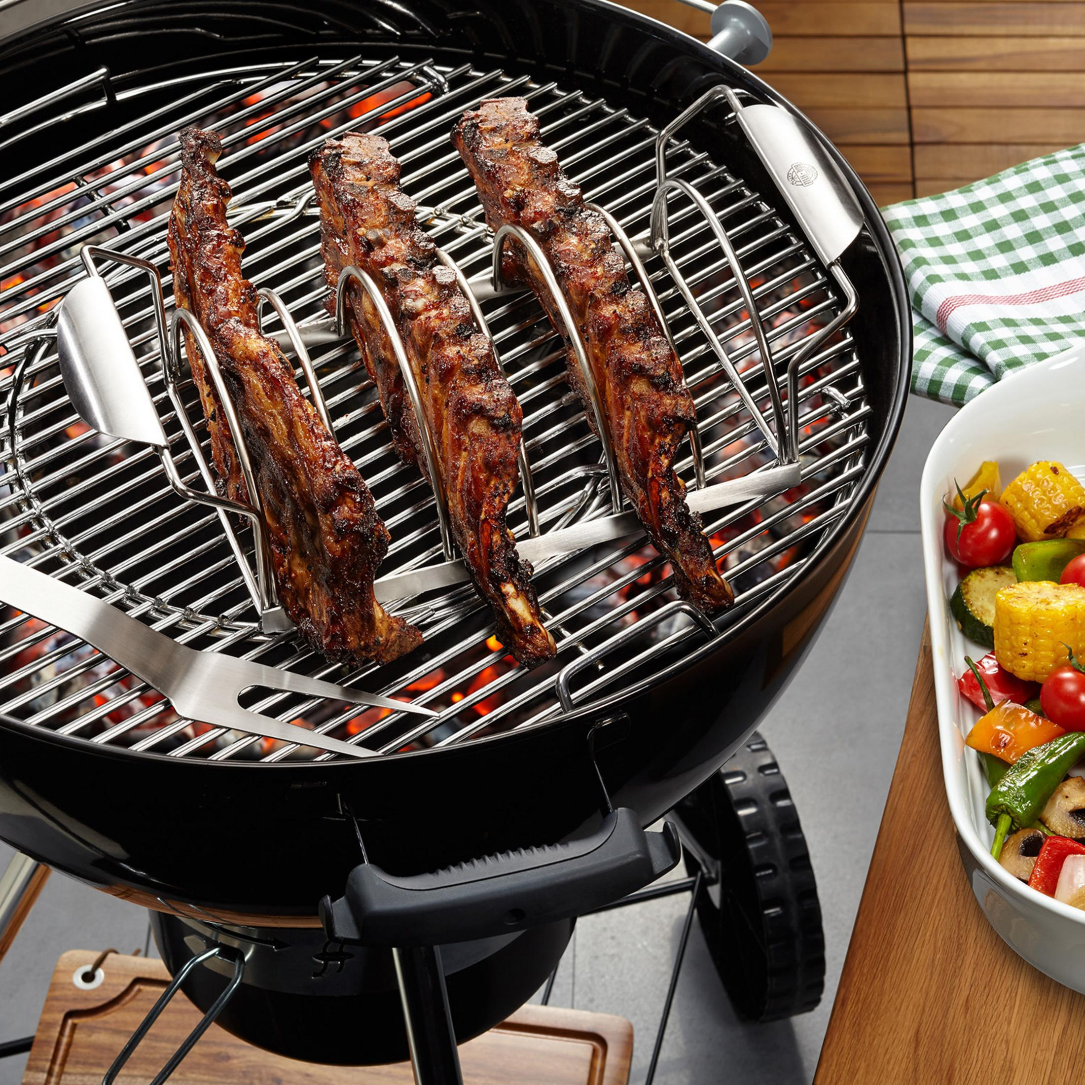 Gegrillte Rippchen auf einem Grill, mit Gemüse in einer Schüssel. Der Grill ist schwarz.