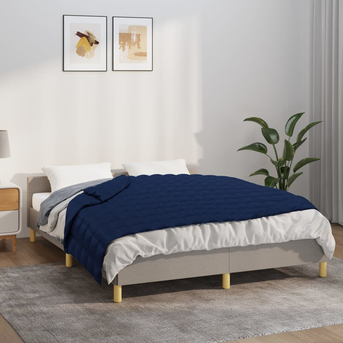 Schlafzimmer mit Bett, dunkelblauer Steppdecke und zwei gerahmten Bildern.