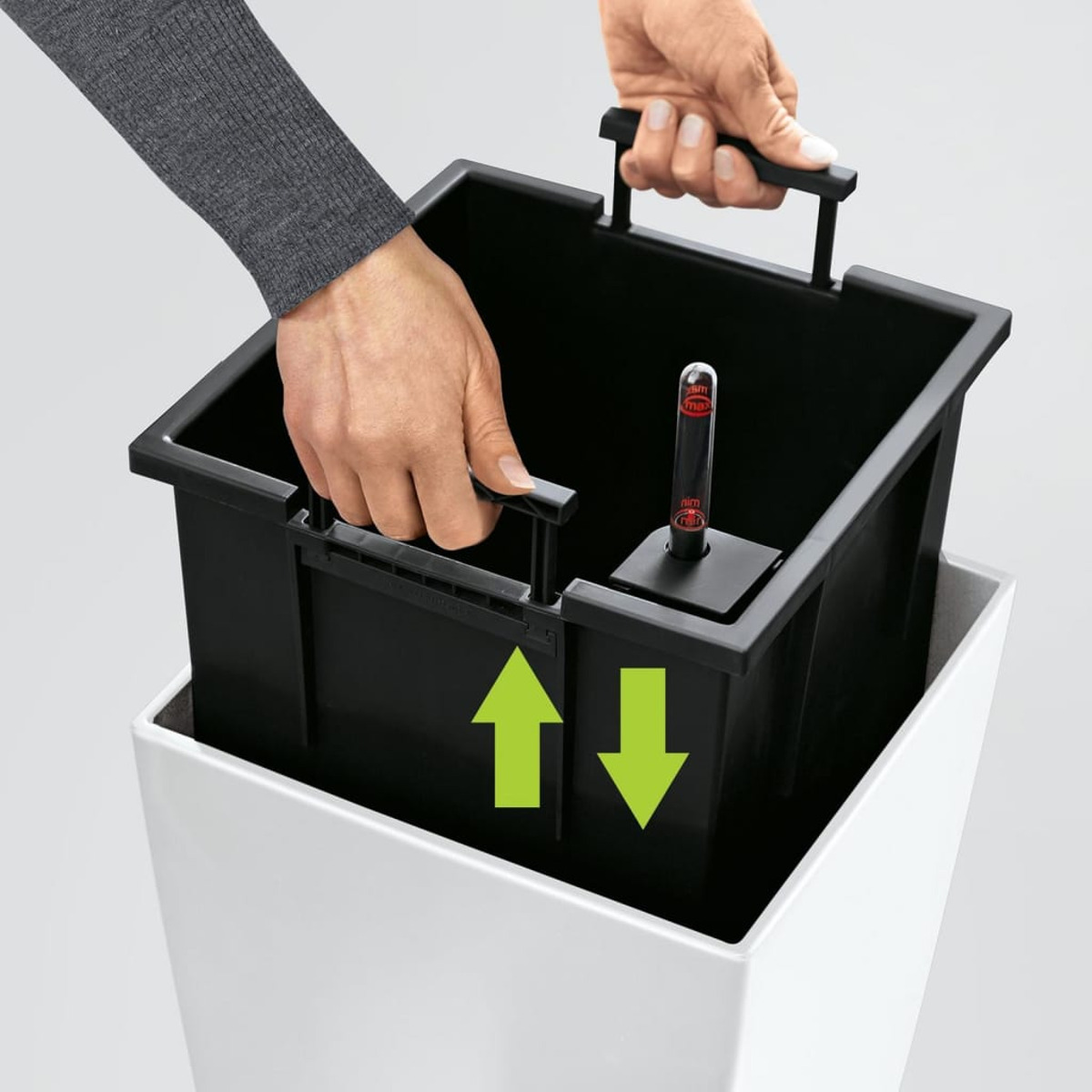 Hände, die einen schwarzen Innenbehälter in einen weißen Außentopf setzen. Grüne Pfeile sind zu sehen.