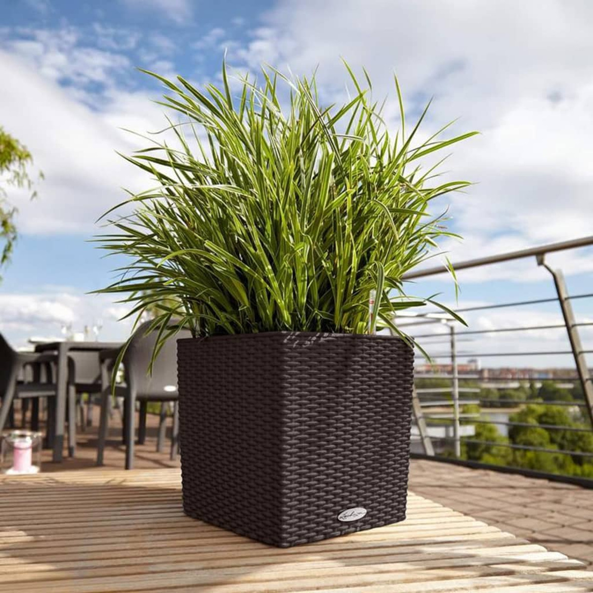 Jardinière carrée marron avec plantes vertes sur une terrasse en bois.