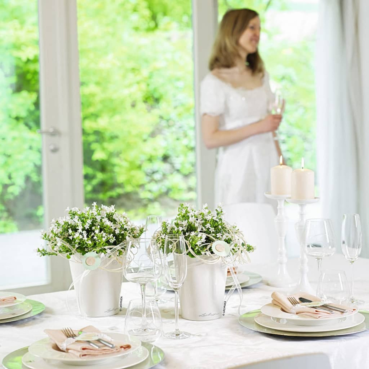 Ein Hochzeitstisch mit Blumen, Gläsern, Kerzen und einer Frau im Hintergrund.