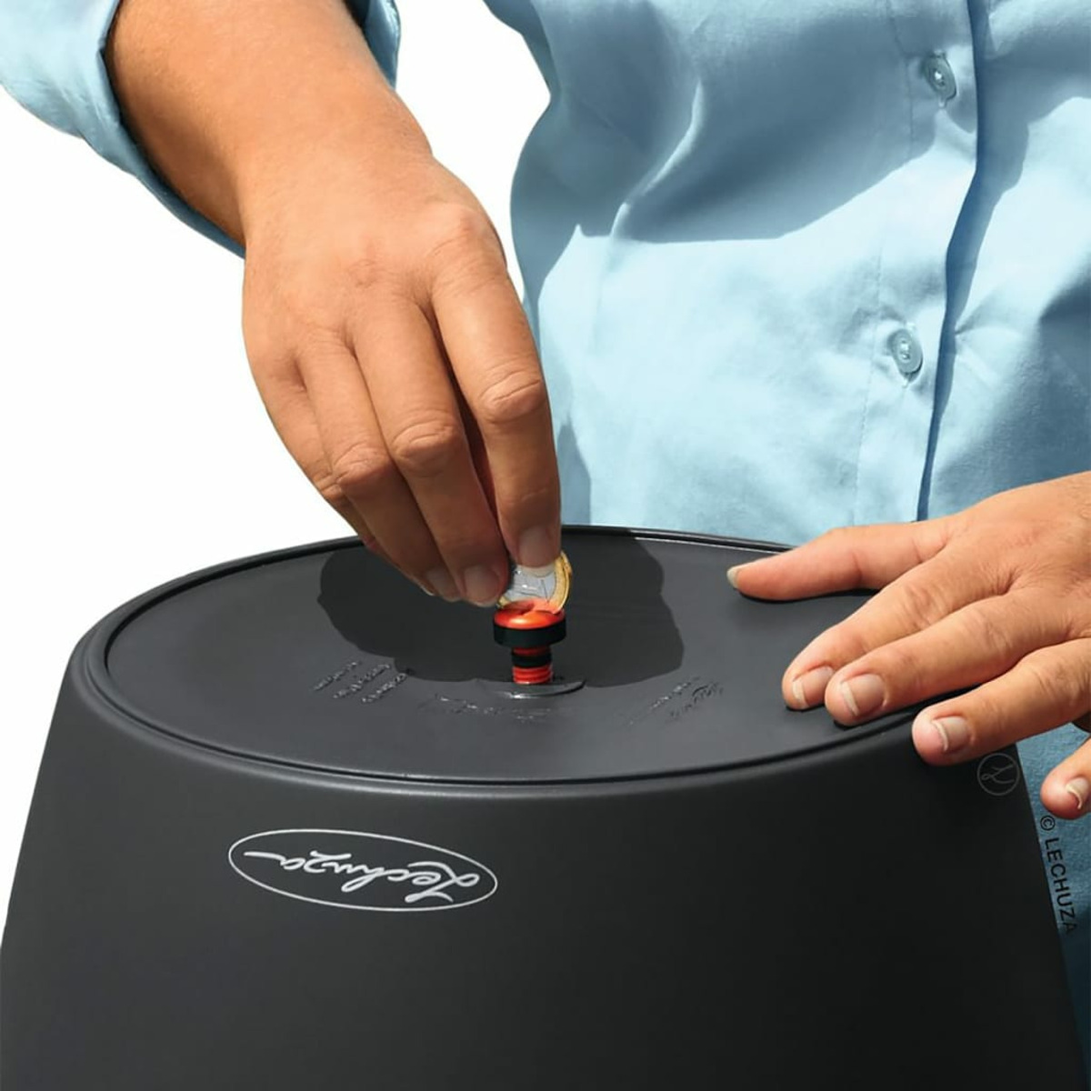 Main plaçant une pièce sur un pot noir Lechuza. Le pot a un indicateur de niveau d'eau.