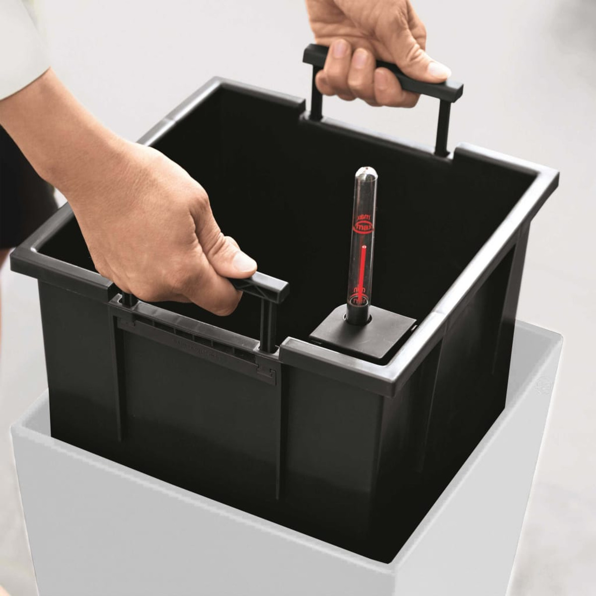 Mains tenant un insert de jardinière noir. Flotteur rouge indique le niveau d'eau.