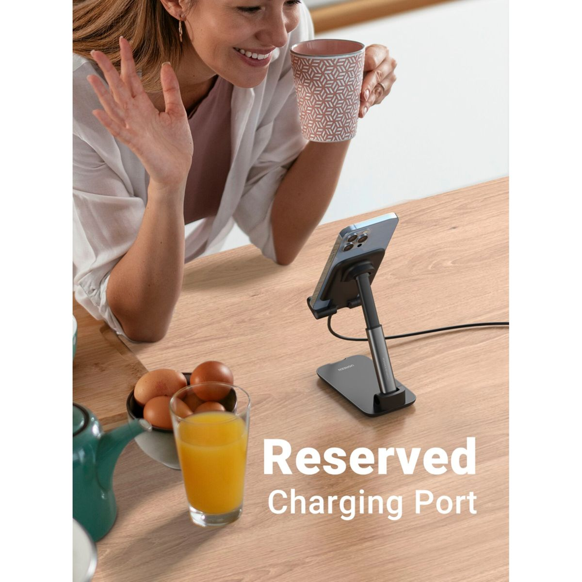 Kobieta trzymająca kubek obok stojaka na telefon z portem ładowania i jajkami.