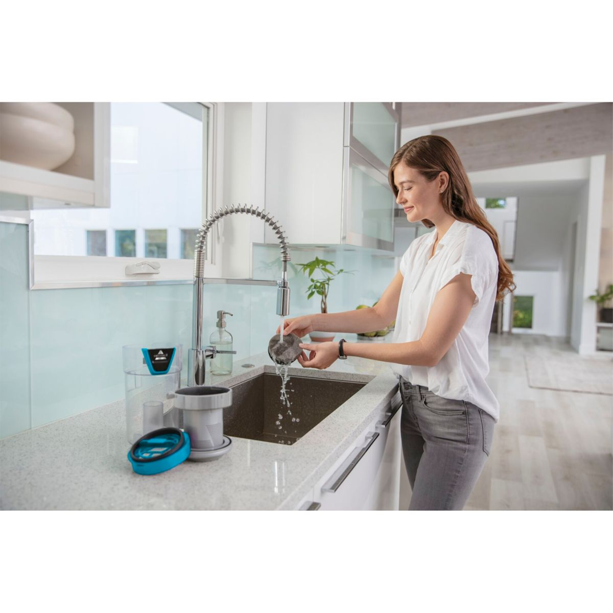 Donna che lava un filtro sotto un rubinetto, in una cucina moderna.