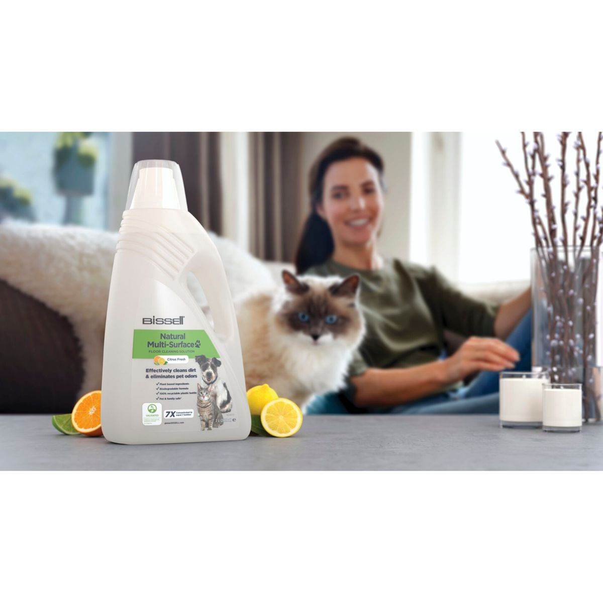 Een fles allesreiniger met een vrouw, kat, citroenen en sinaasappel op de achtergrond.