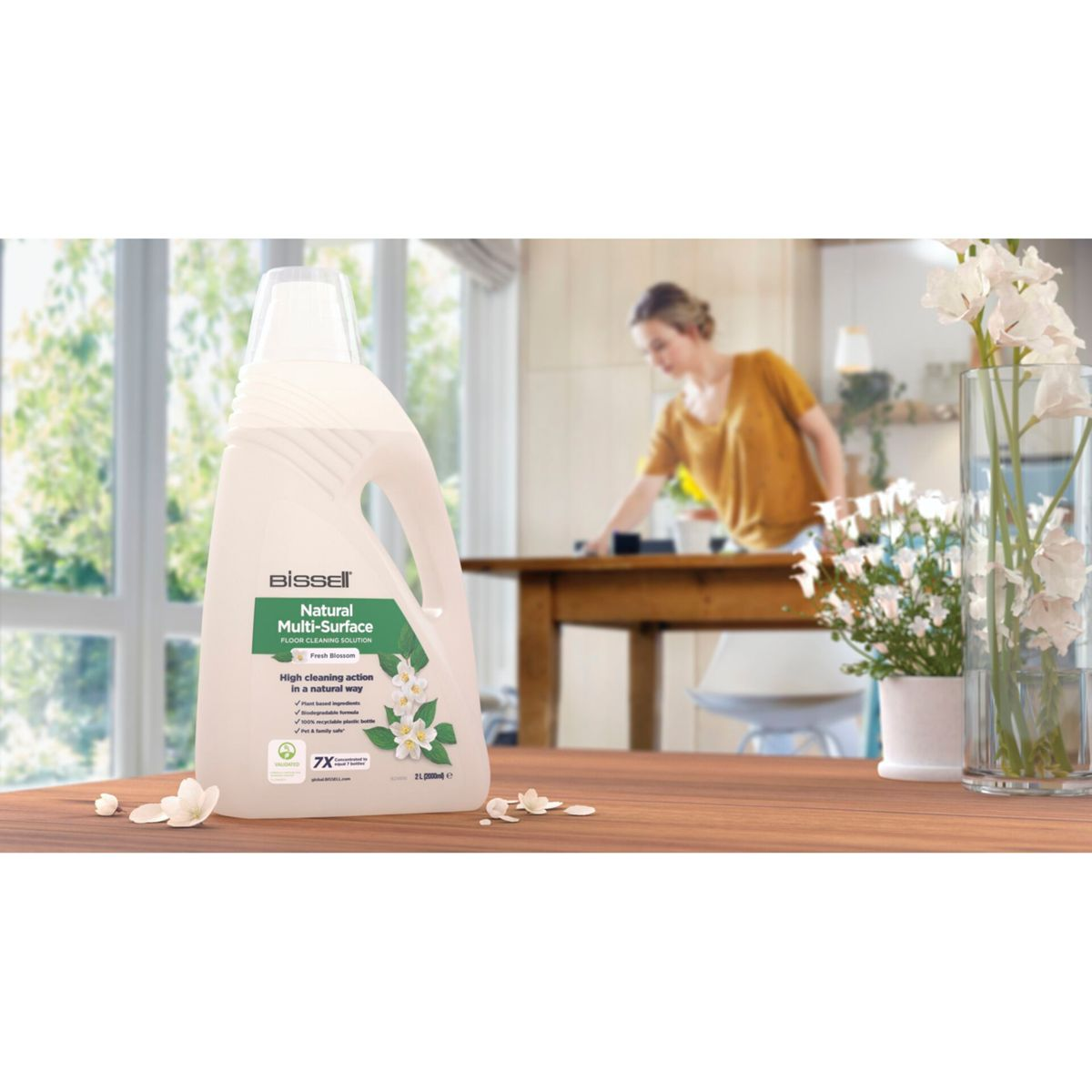 Bottiglia di detergente per pavimenti e donna che pulisce un tavolo di legno in cucina.