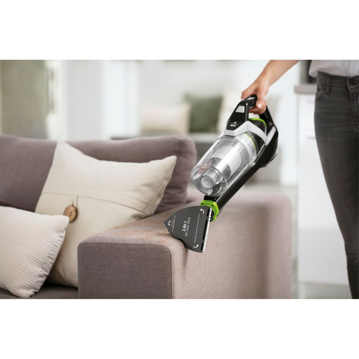 Eine Person benutzt einen Handstaubsauger auf einem Sofa. Der Staubsauger reinigt einen Fleck.