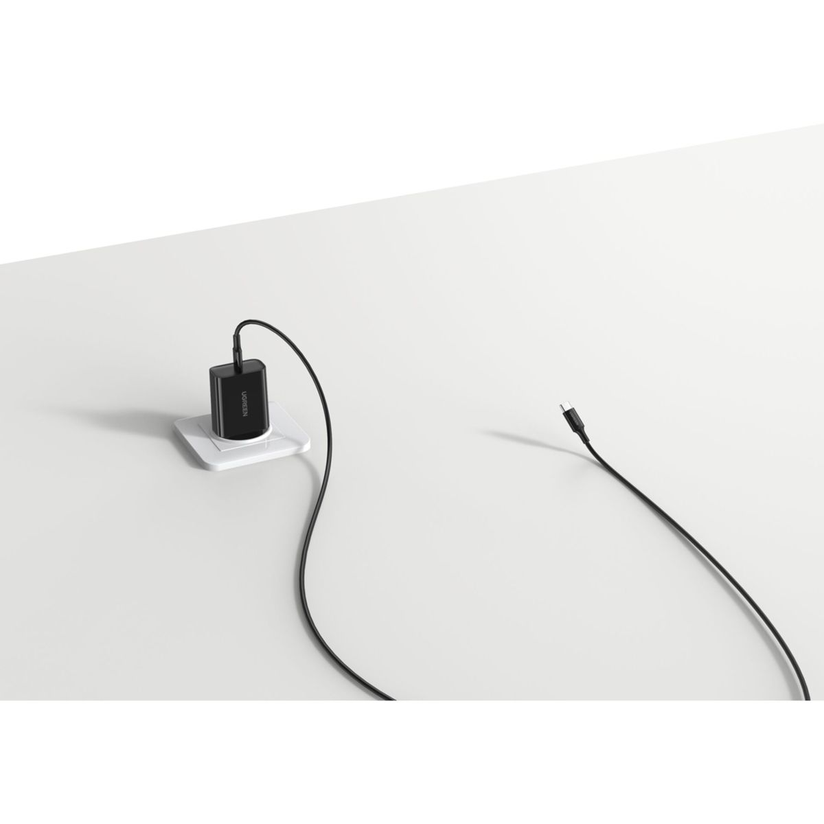 Czarna ładowarka w białym gniazdku, z czarnym kablem.