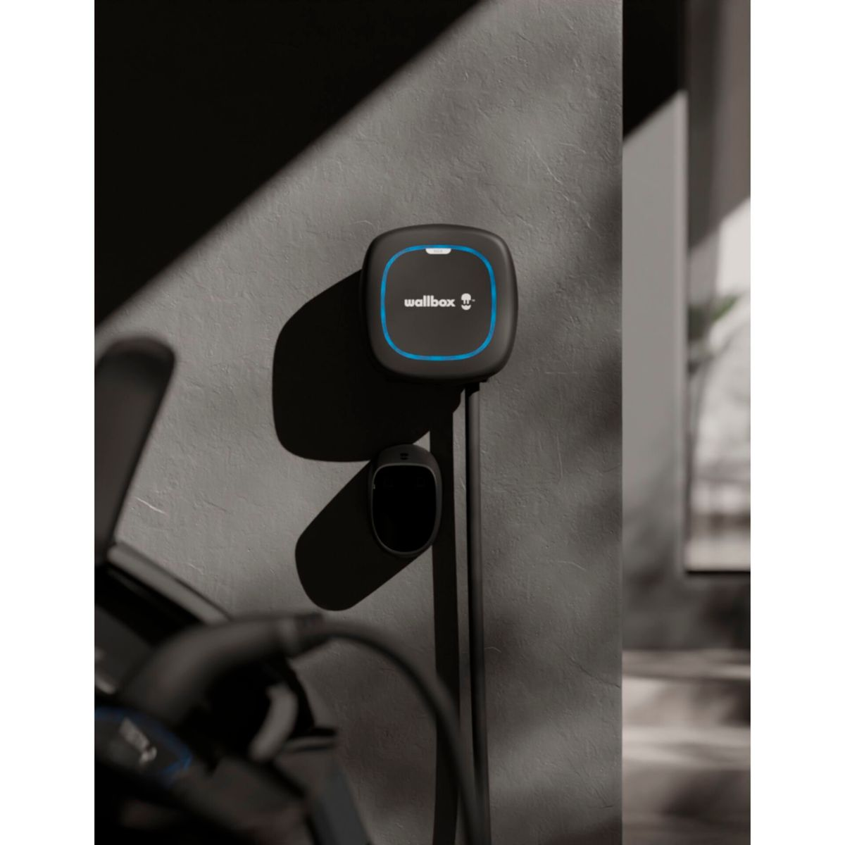 Ein schwarzes Elektroauto-Ladegerät, das an einer grauen Wand montiert ist. Das Ladegerät hat eine blaue Umrandung.