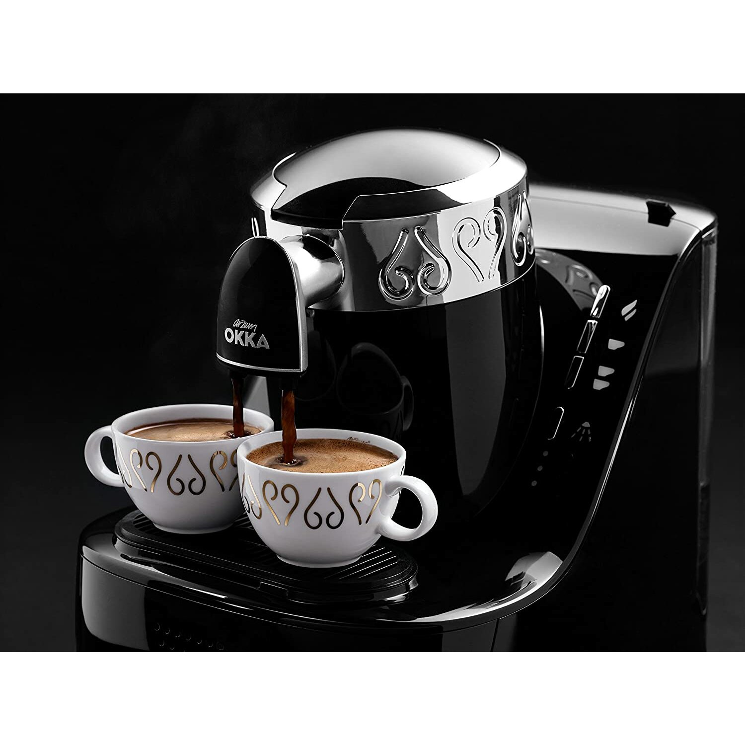 Kaffeemaschine gießt Kaffee in zwei Tassen. Die Tassen haben goldene Muster. Schwarzer Hintergrund.