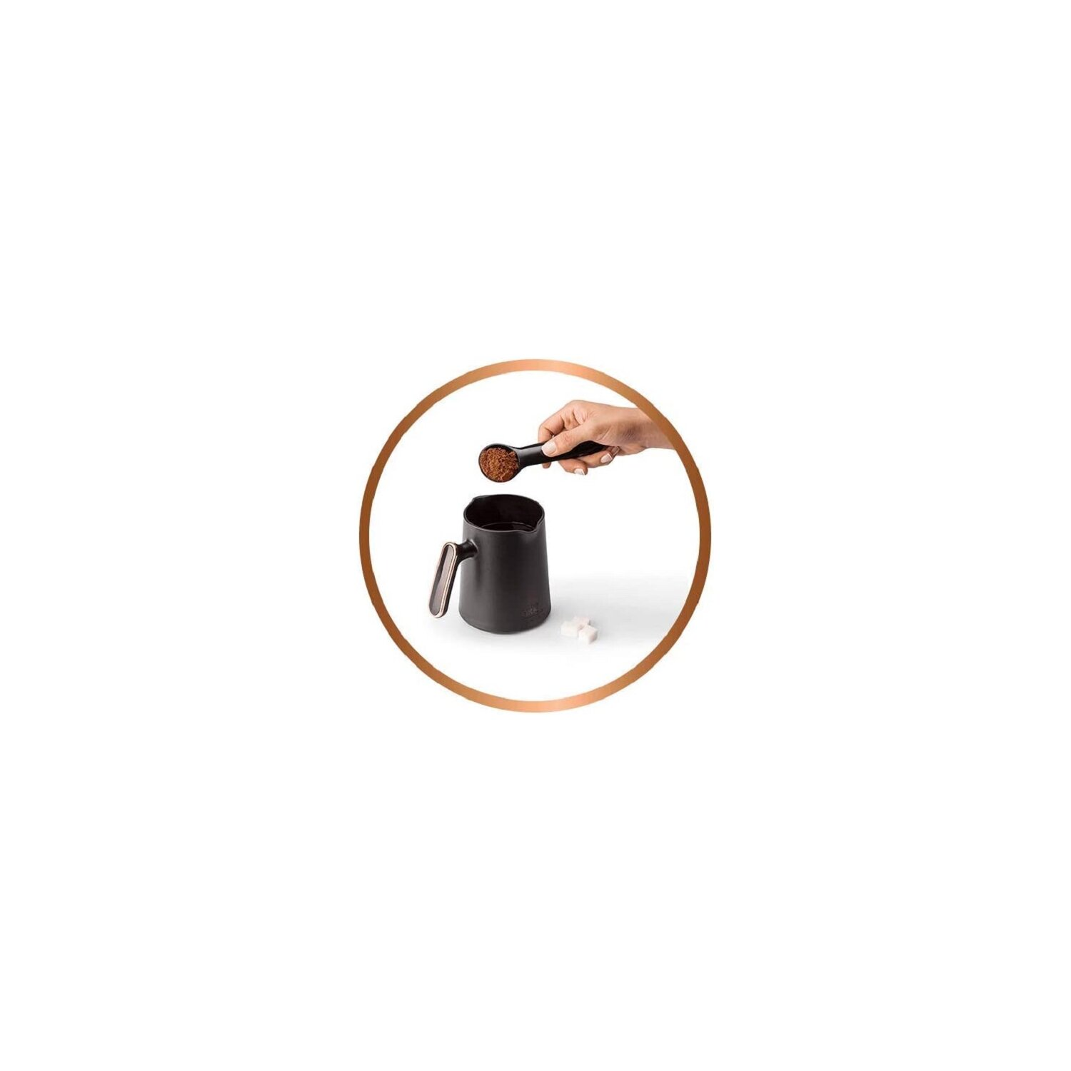 Eine Hand, die einen Löffel hält, gießt Kaffeepulver in einen schwarzen Becher. Zwei Zuckerwürfel liegen daneben.