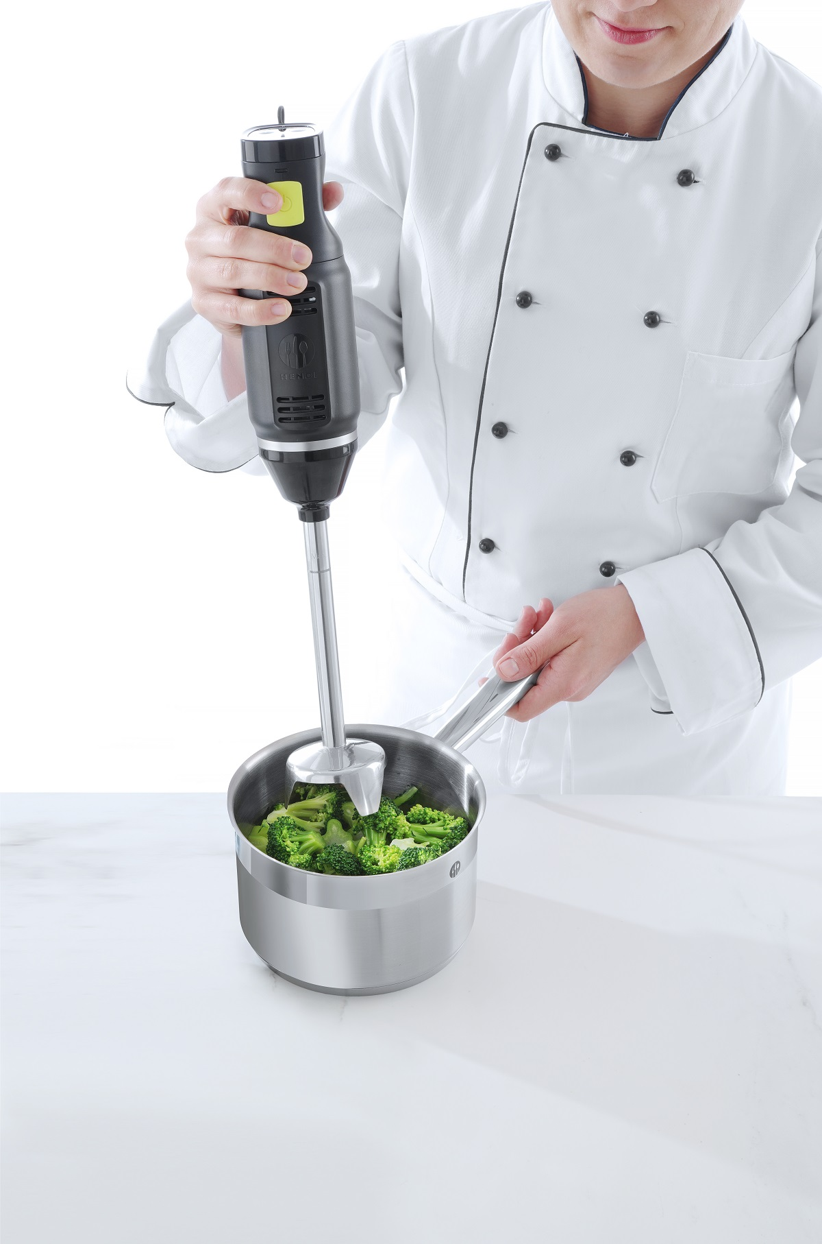 Ein Koch, der einen Stabmixer in einem Topf mit Brokkoli verwendet.