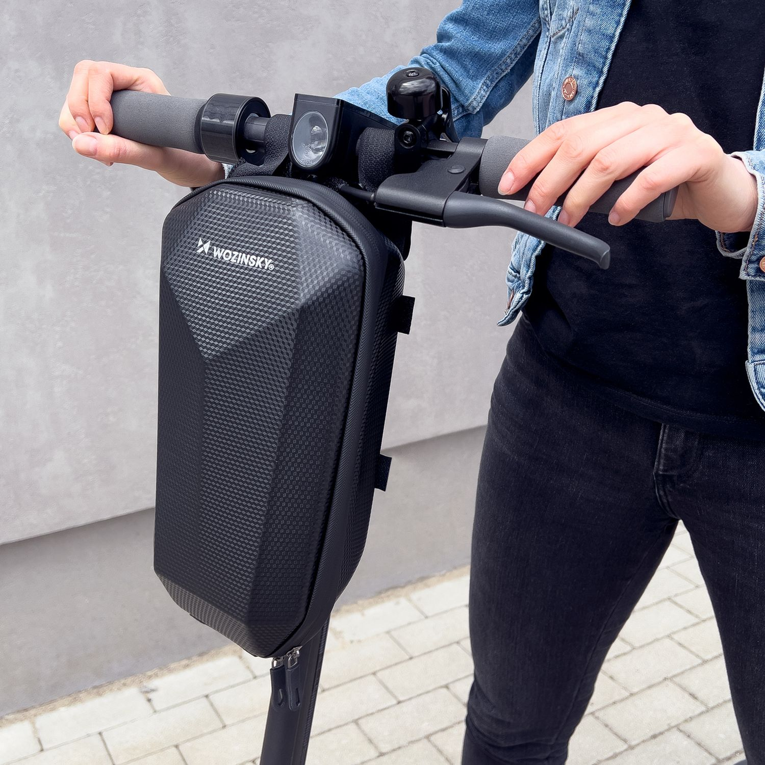 Person hält eine schwarze Scooter-Tasche mit WoZinsky-Logo. Die Tasche ist an einem Roller befestigt.