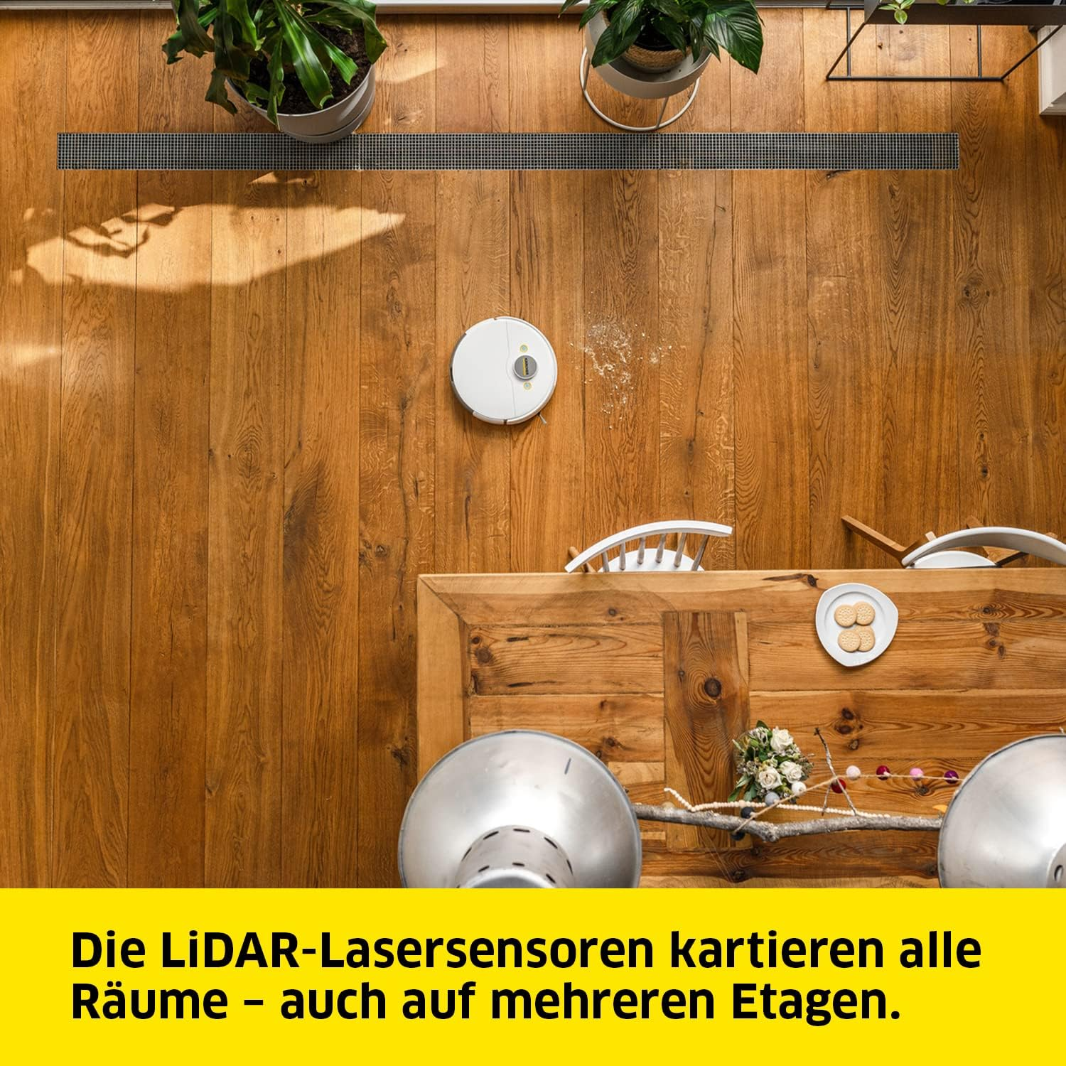 Robot sprzątający na drewnianej podłodze. Widoczny stół i rośliny.