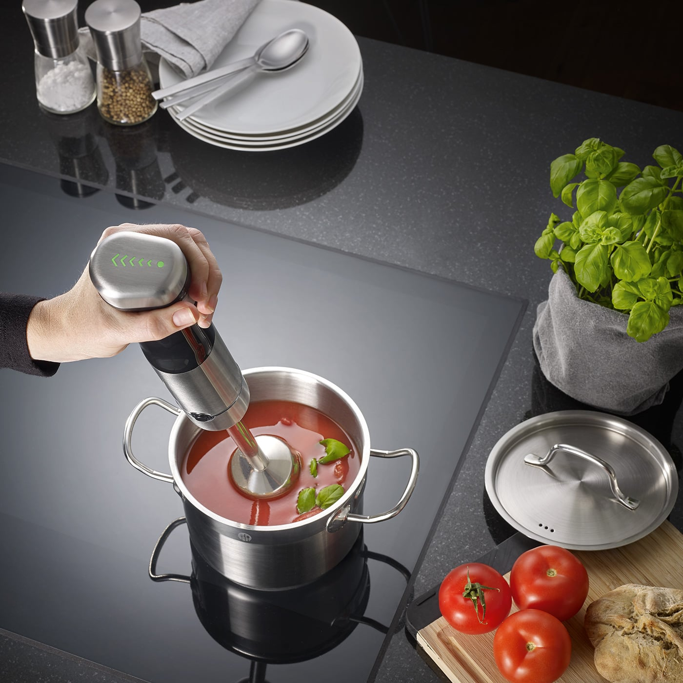 Mano usa un frullatore a immersione in zuppa di pomodoro. Pomodori e basilico vicini.