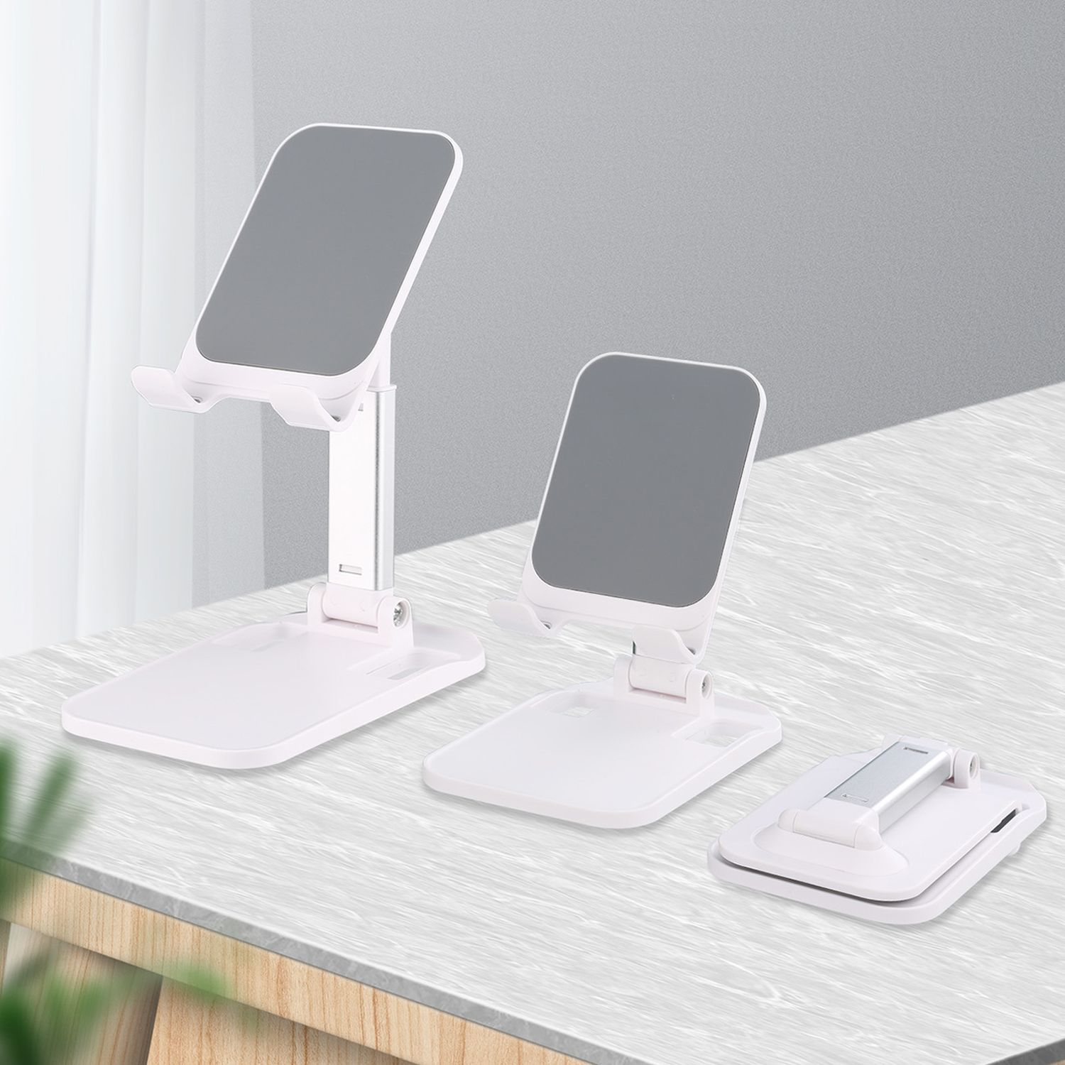 Trzy białe stojaki na telefon. Dwa są pionowe, jeden złożony. Wszystkie na jasnoszarej powierzchni.