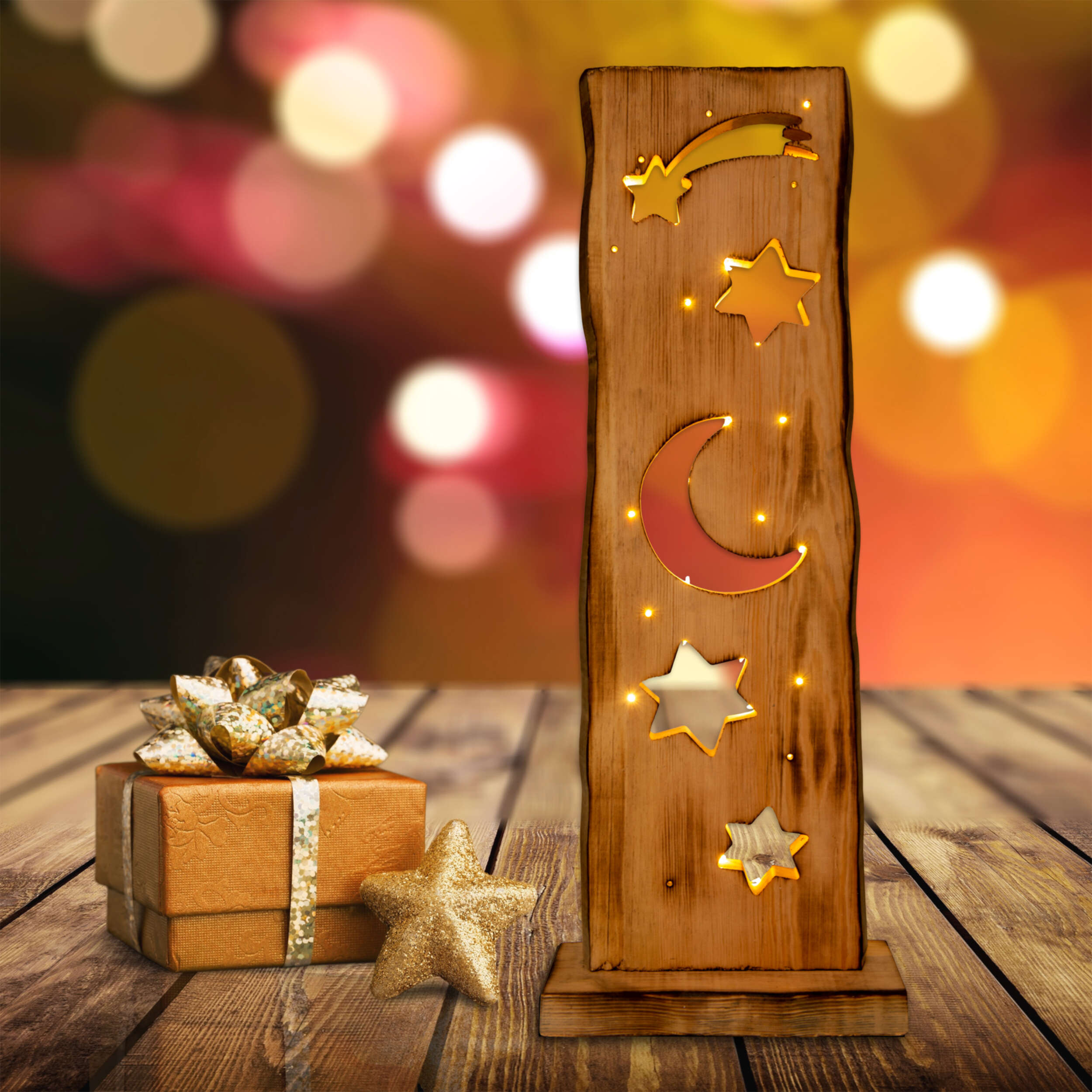 Dekoratives Holzstück mit goldenen Sternen und Mond. Eine Geschenkbox und ein Stern sind davor.