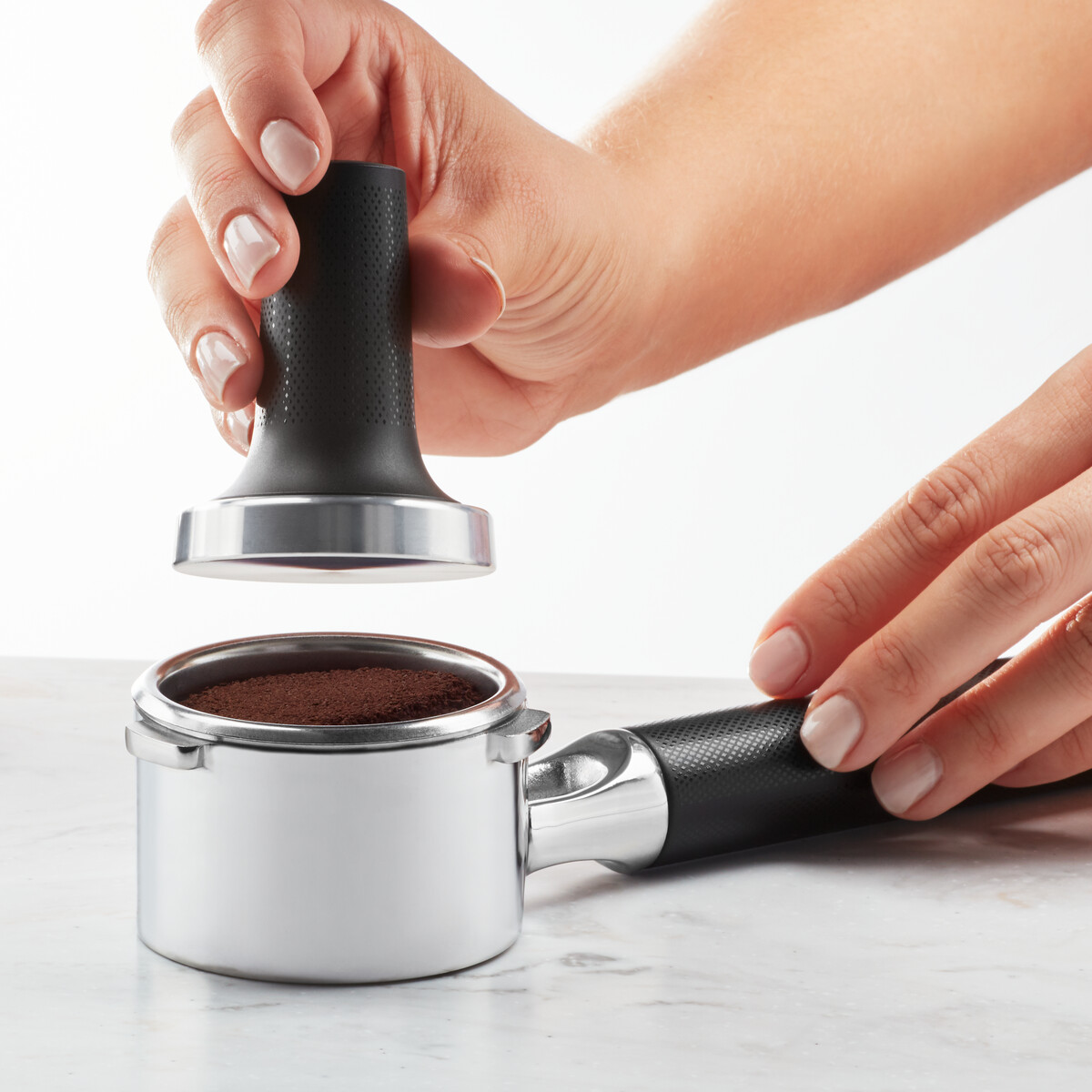Hände, die Kaffeepulver in einem Siebträger mit einem schwarzen Tamper verdichten.